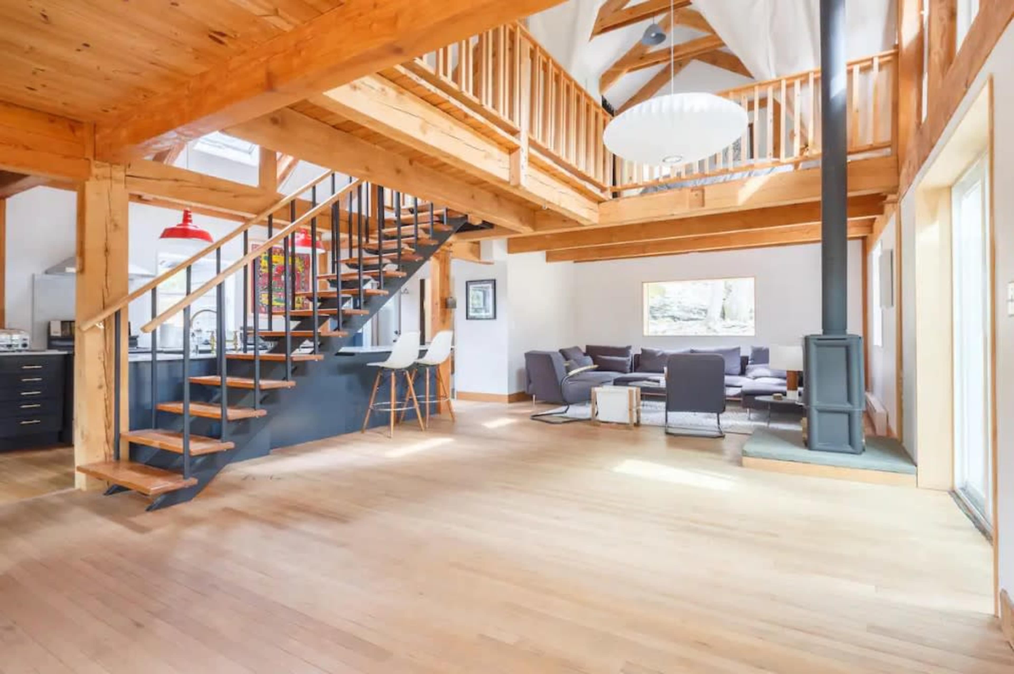 The image shows a spacious, modern interior featuring wooden beams, an open living area, and a staircase leading to a loft.