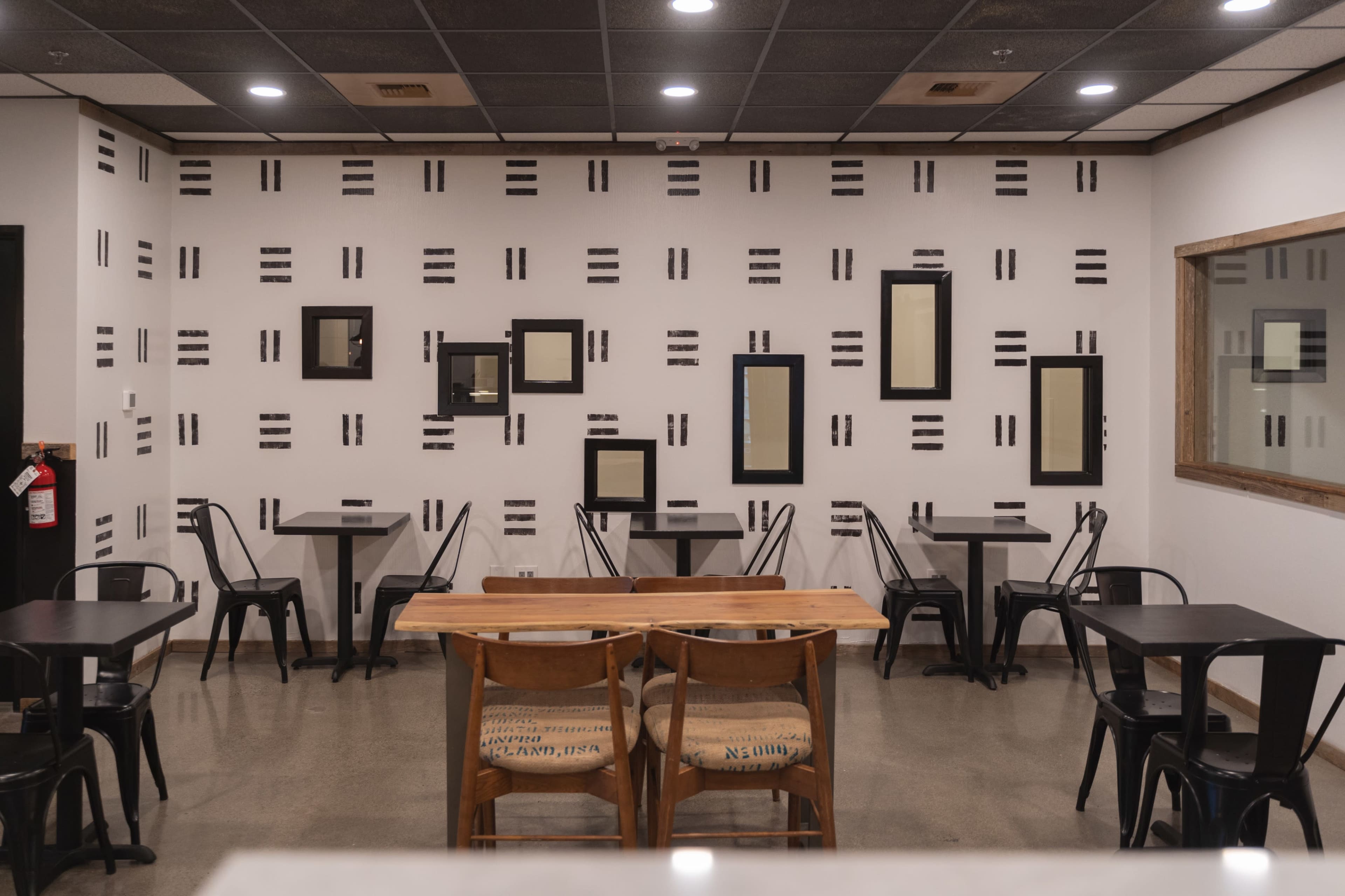 The image shows a cafe interior with scattered tables and a wall adorned with various framed mirrors in black frames.