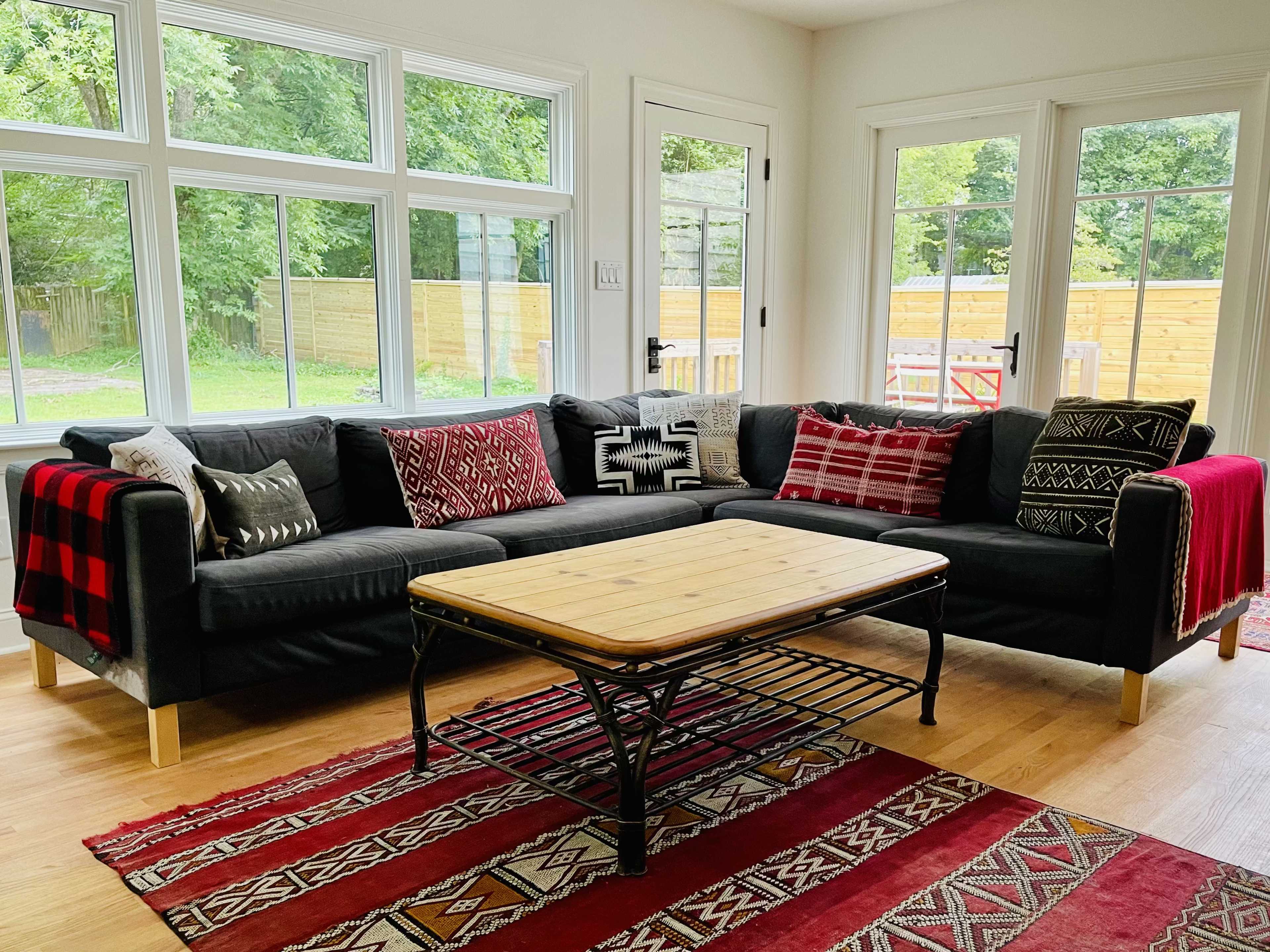 A modern living room features a black sectional sofa adorned with patterned pillows and a wooden coffee table on a red area rug.