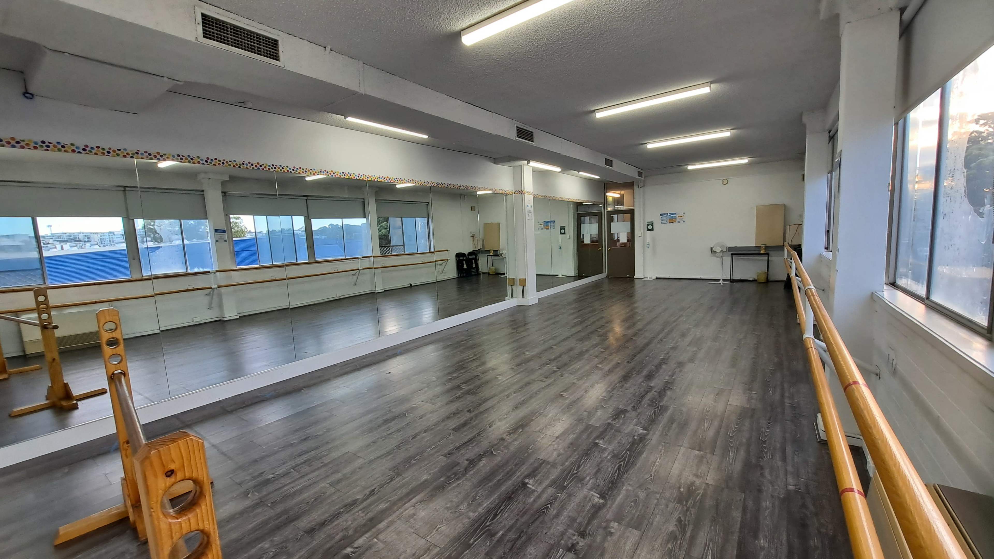 A bright, spacious dance studio with mirrors along one wall and a wooden ballet barre.