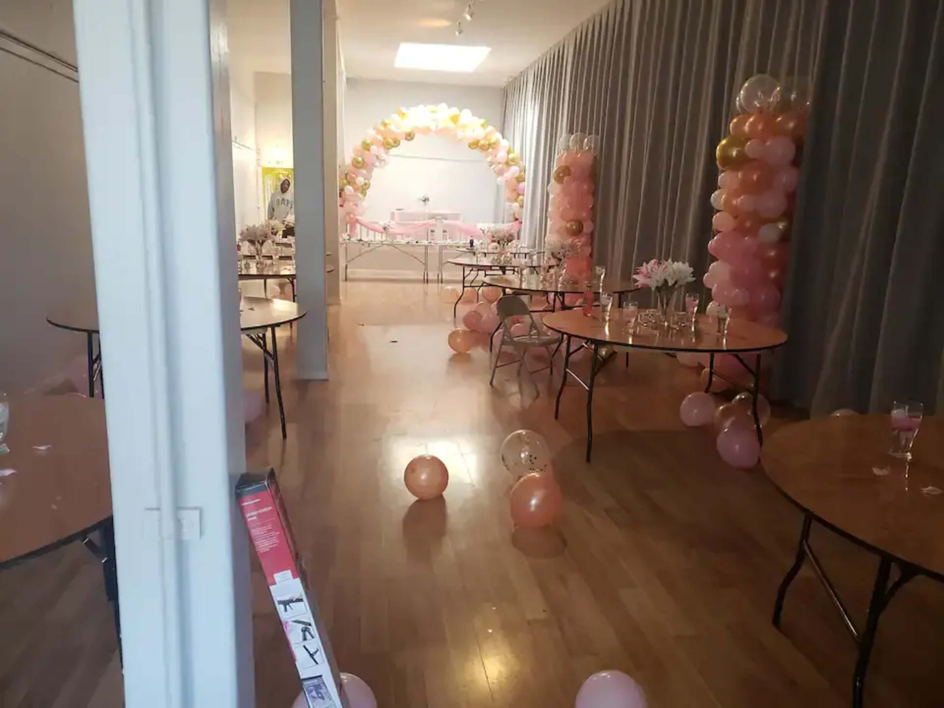 A decorated event space with round tables, balloons, and a centerpiece arrangement.