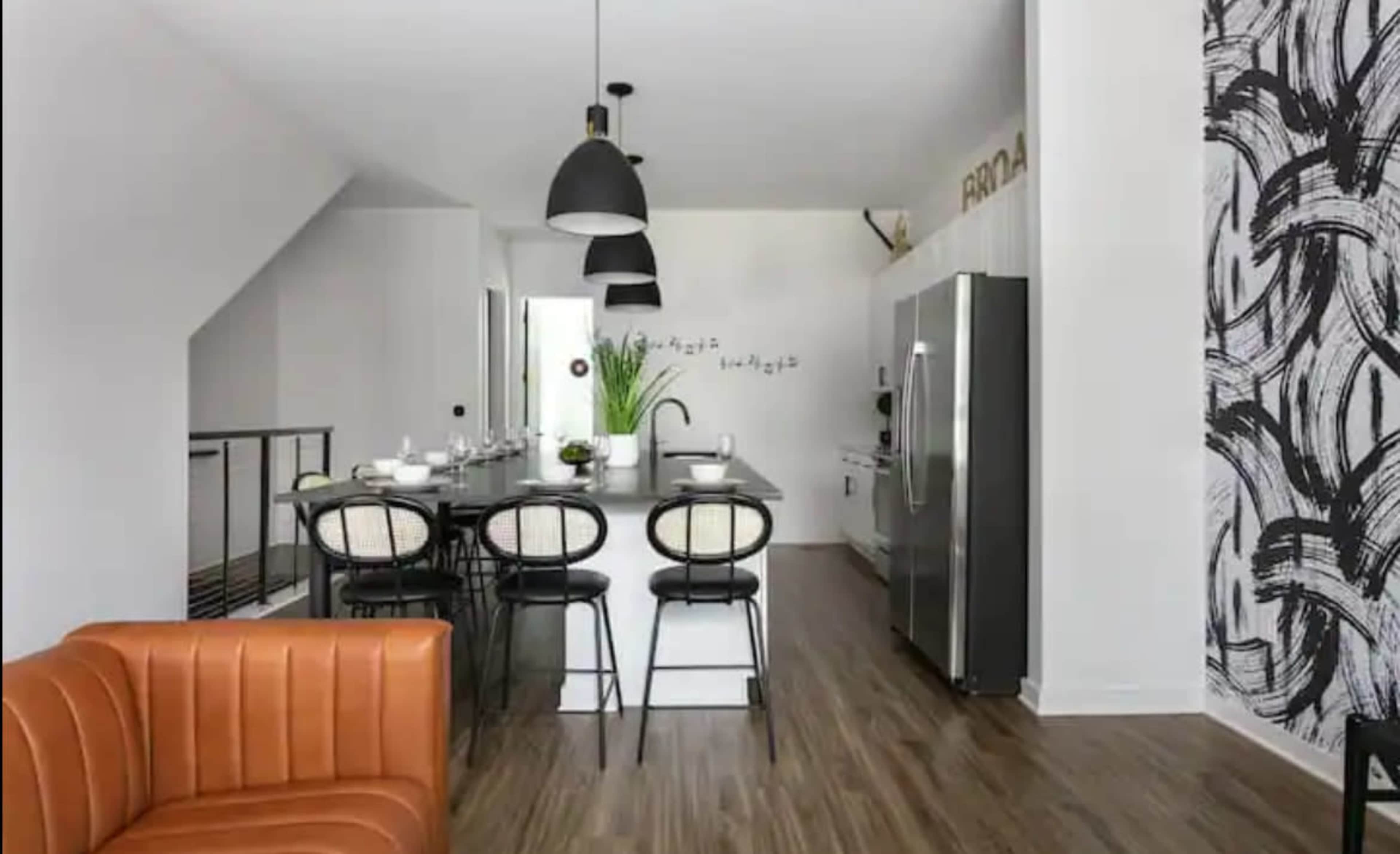 A modern kitchen features a central island with bar stools, stainless steel appliances, and a patterned accent wall.