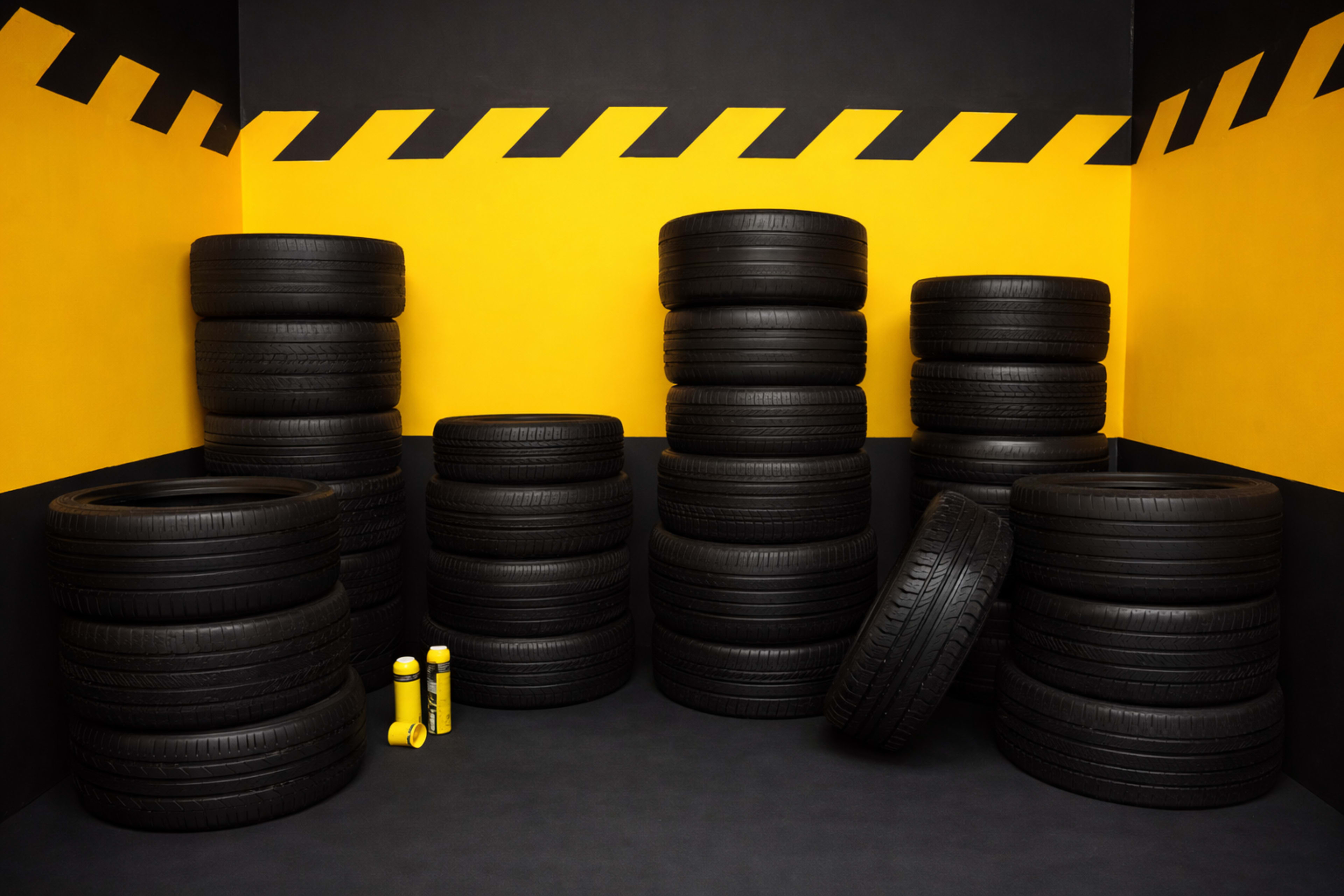 The image shows several stacks of black tires arranged against a yellow and black wall in a corner.