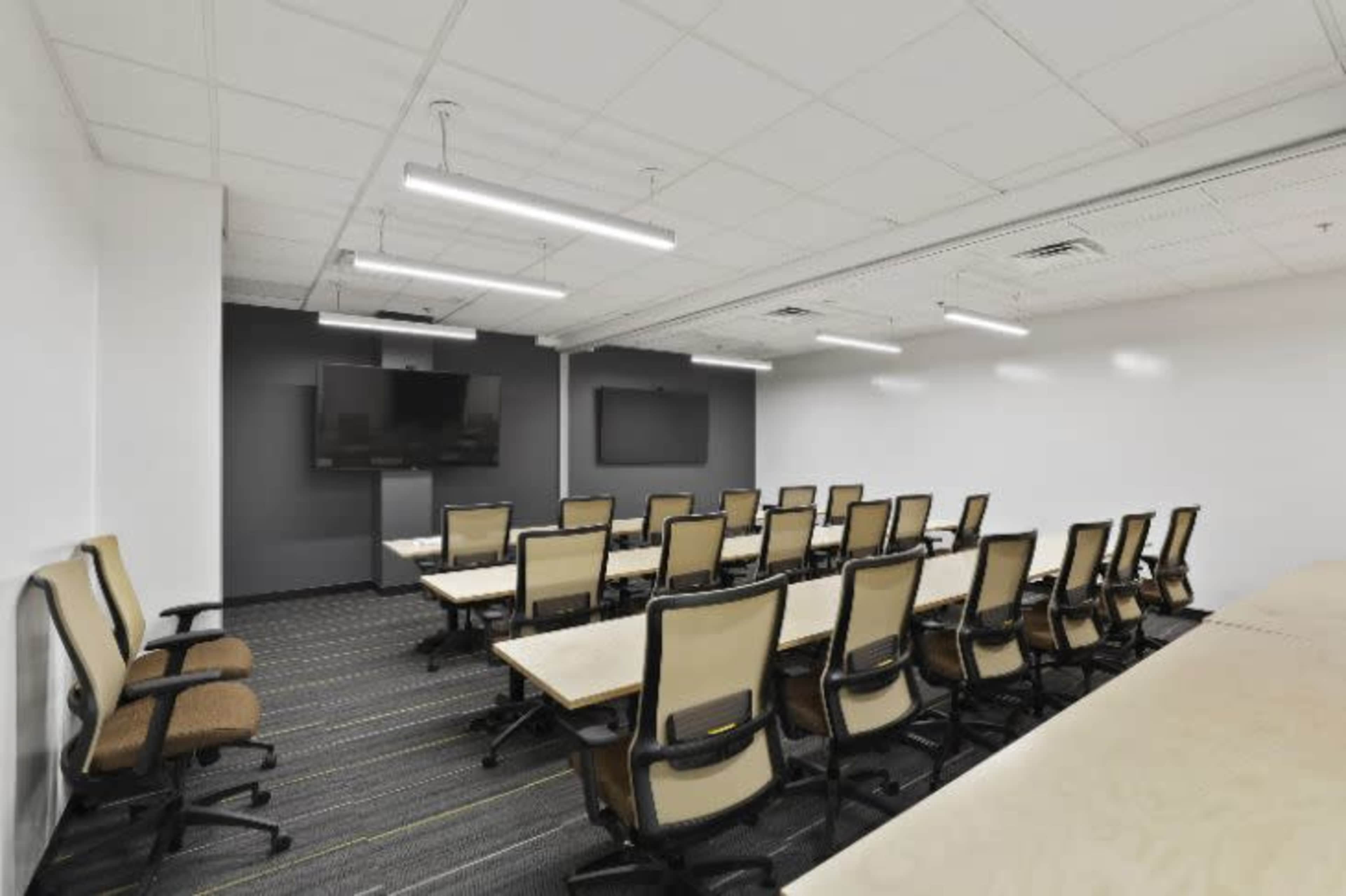 A modern conference room features rows of chairs facing two wall-mounted screens.