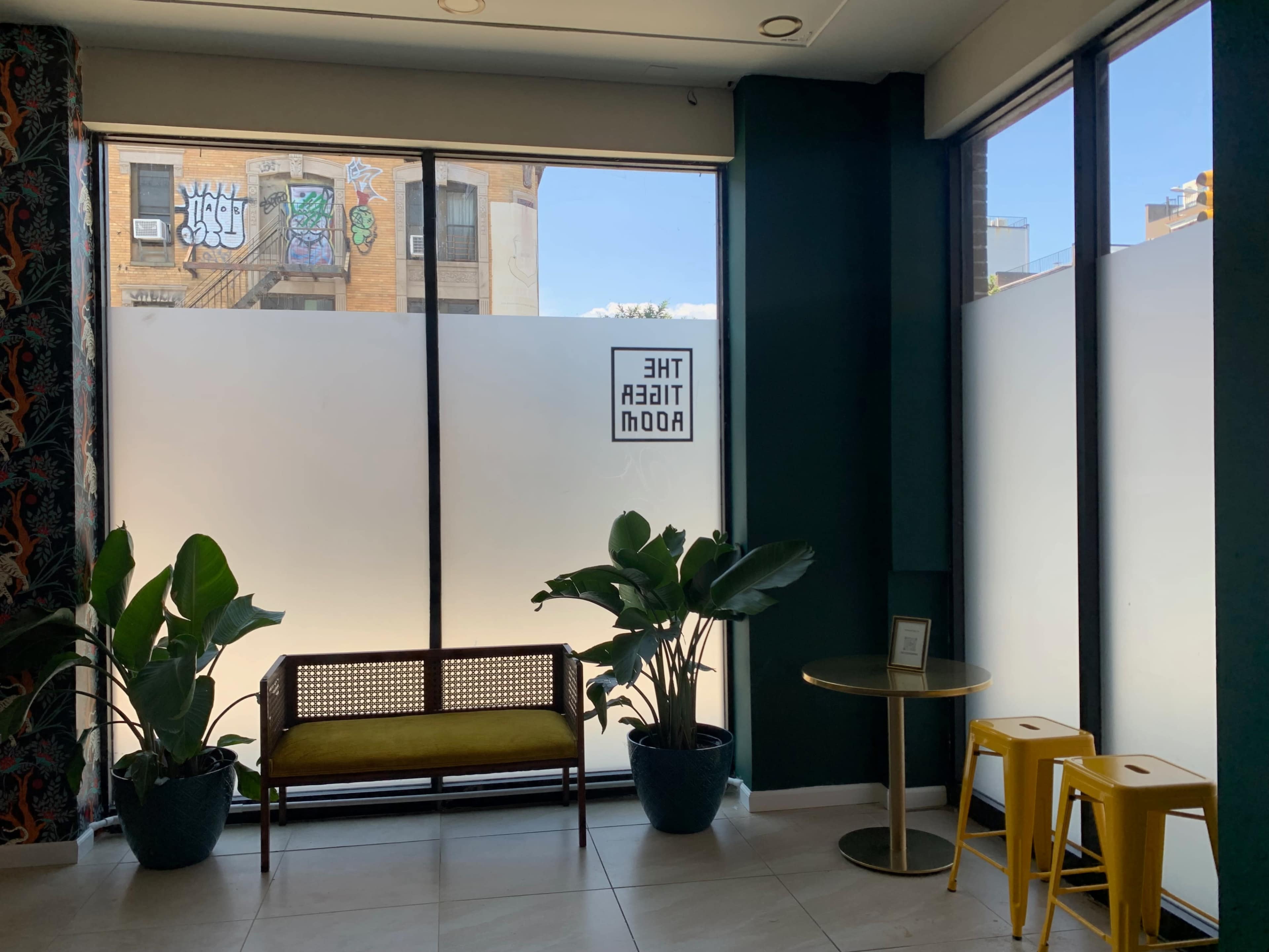 A modern interior space with large windows, a bench, potted plants, and a small round table.