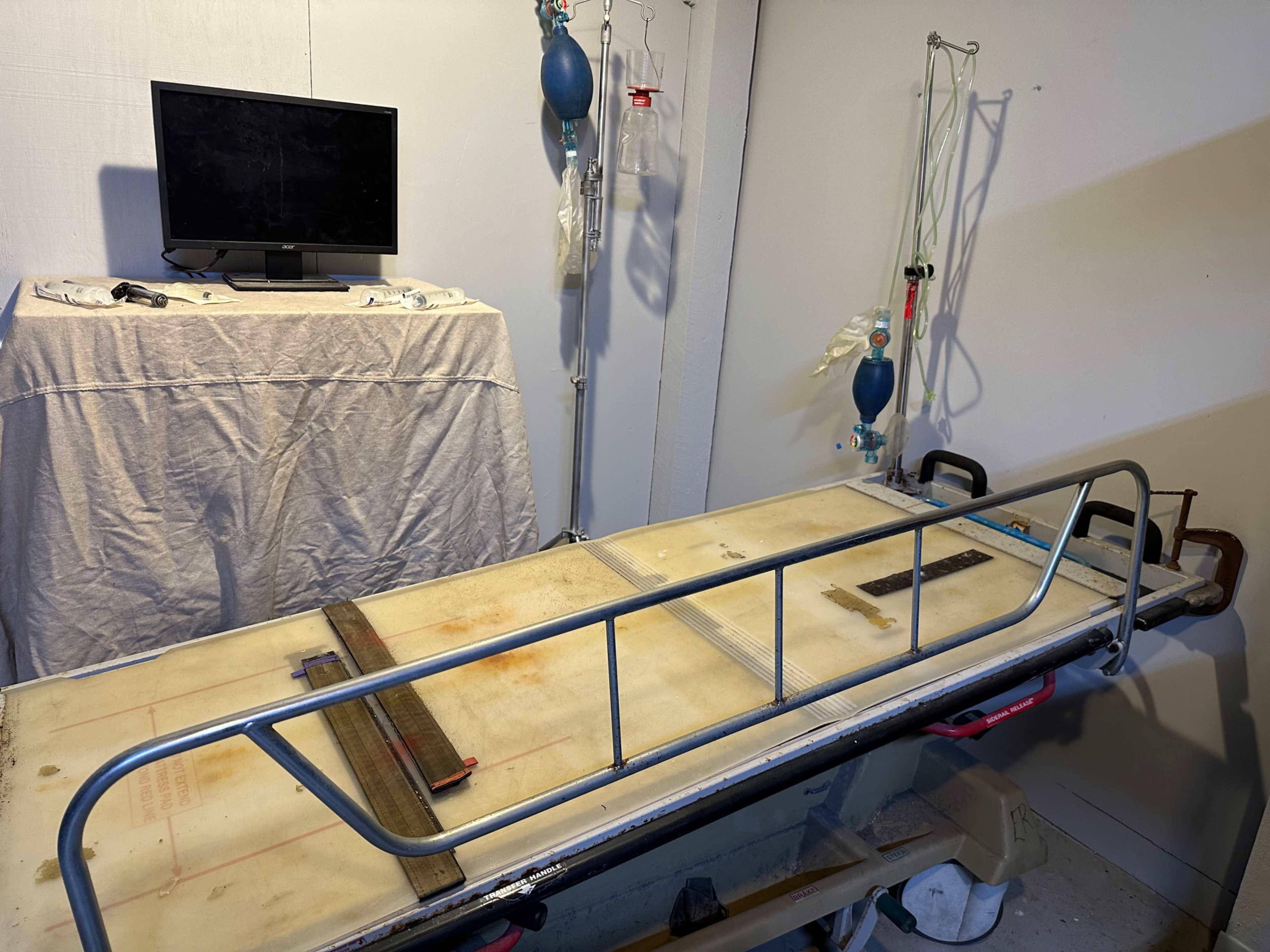 A hospital room with a metal hospital bed positioned in the center, accompanied by medical equipment and a television on a covered table.