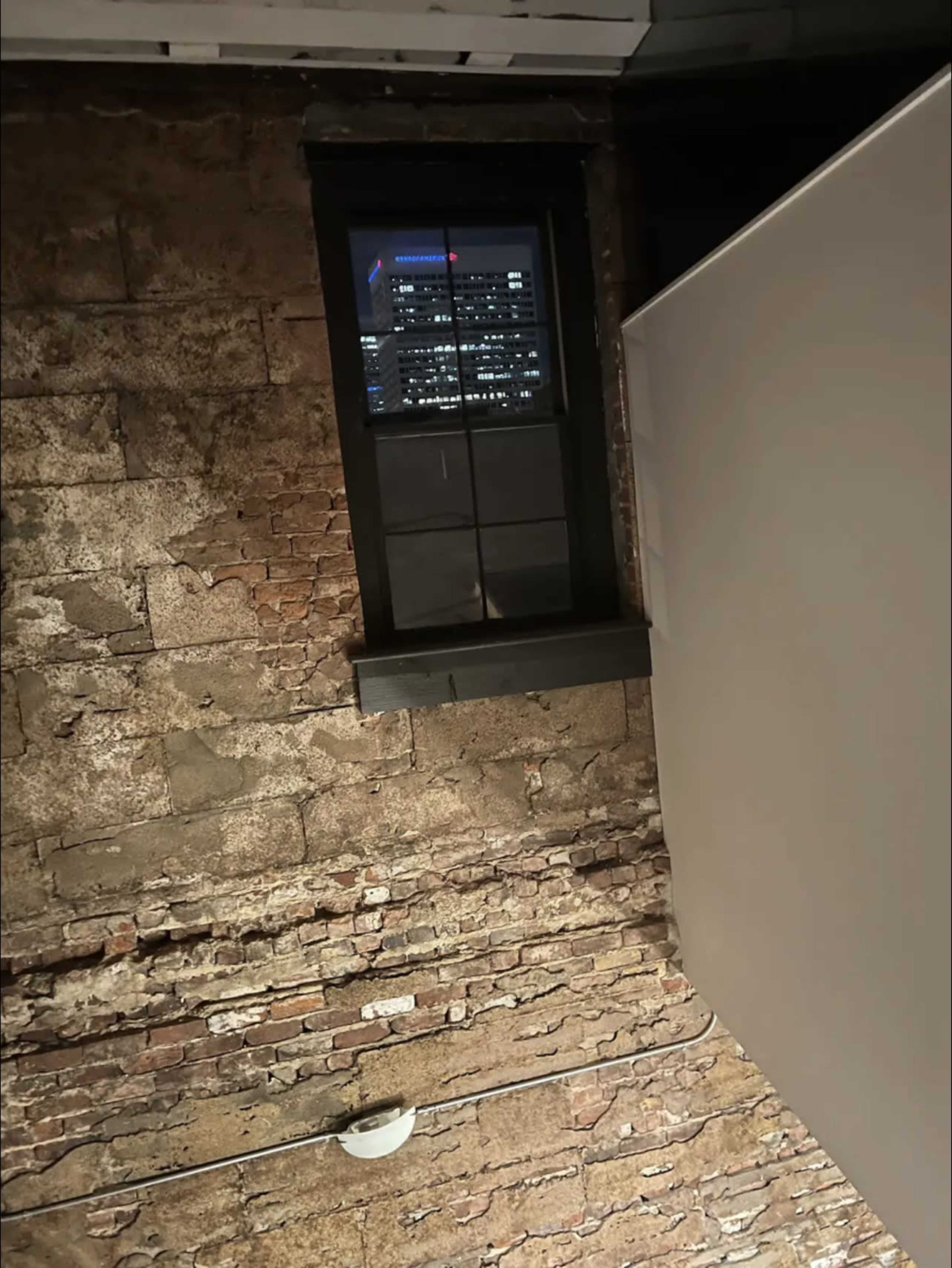 A brick wall with a window in the upper corner, revealing a city skyline in the distance.