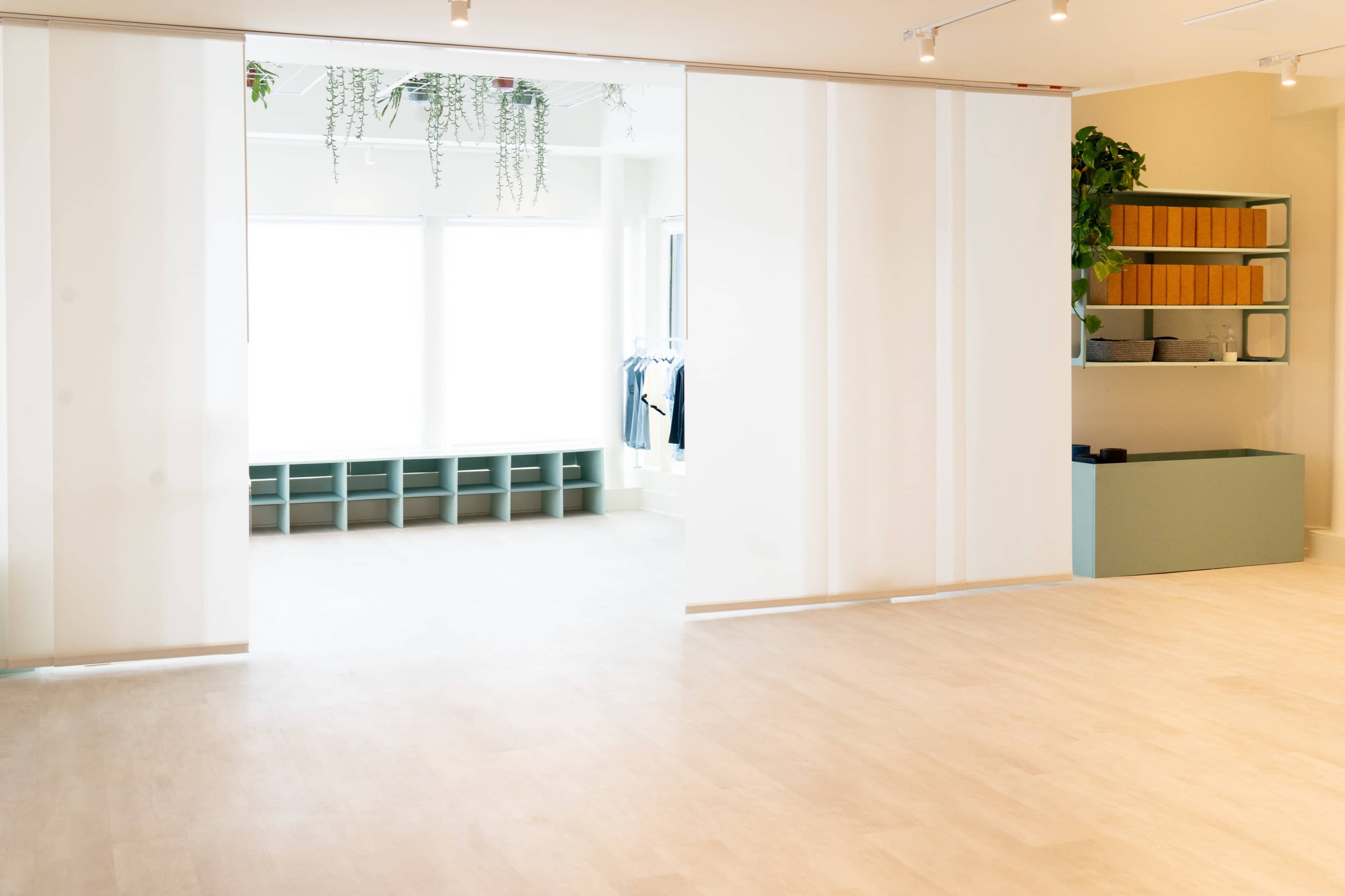 A brightly lit, minimalistic interior space featuring sliding white partitions, green shelving units, and plant decor.