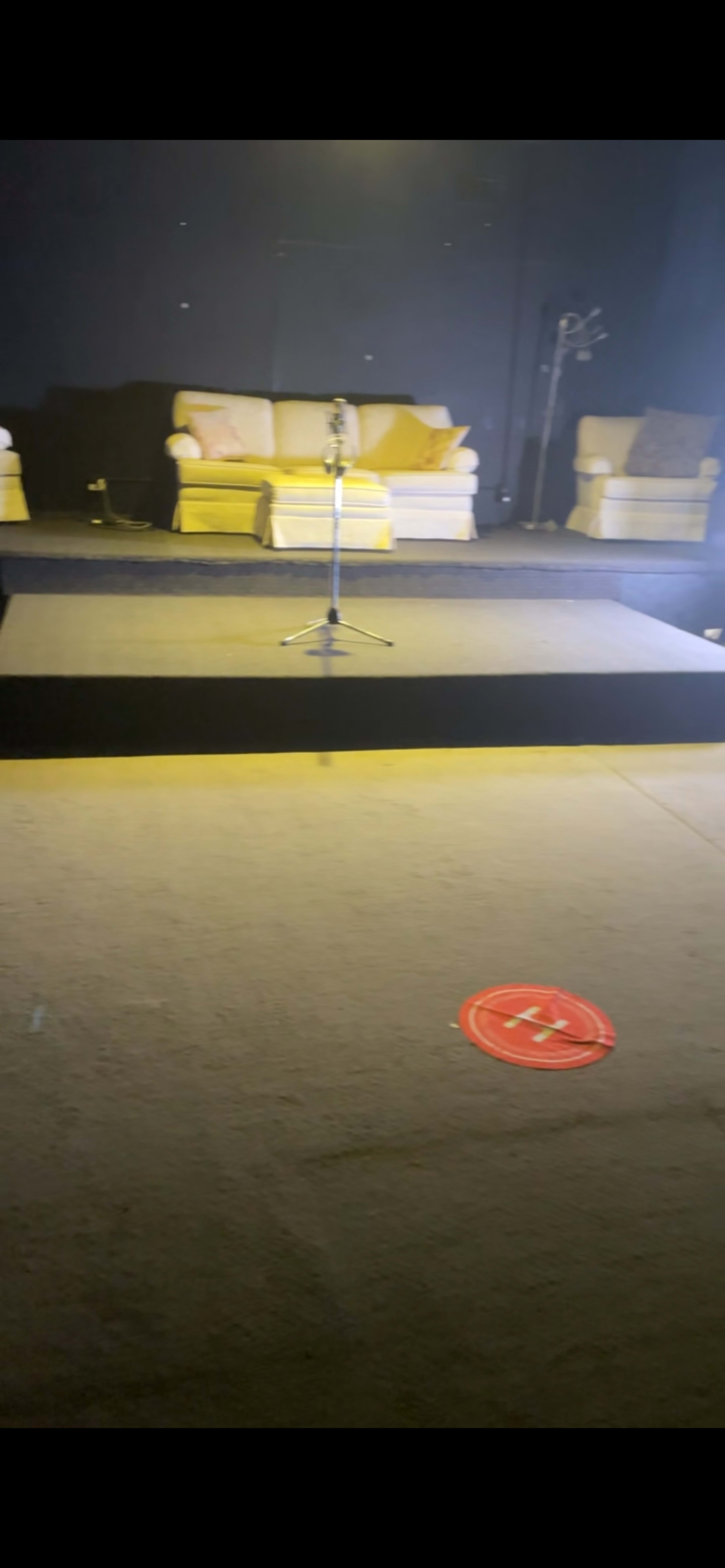 The image shows a small stage with a microphone stand, flanked by two couches, in a dimly lit room.