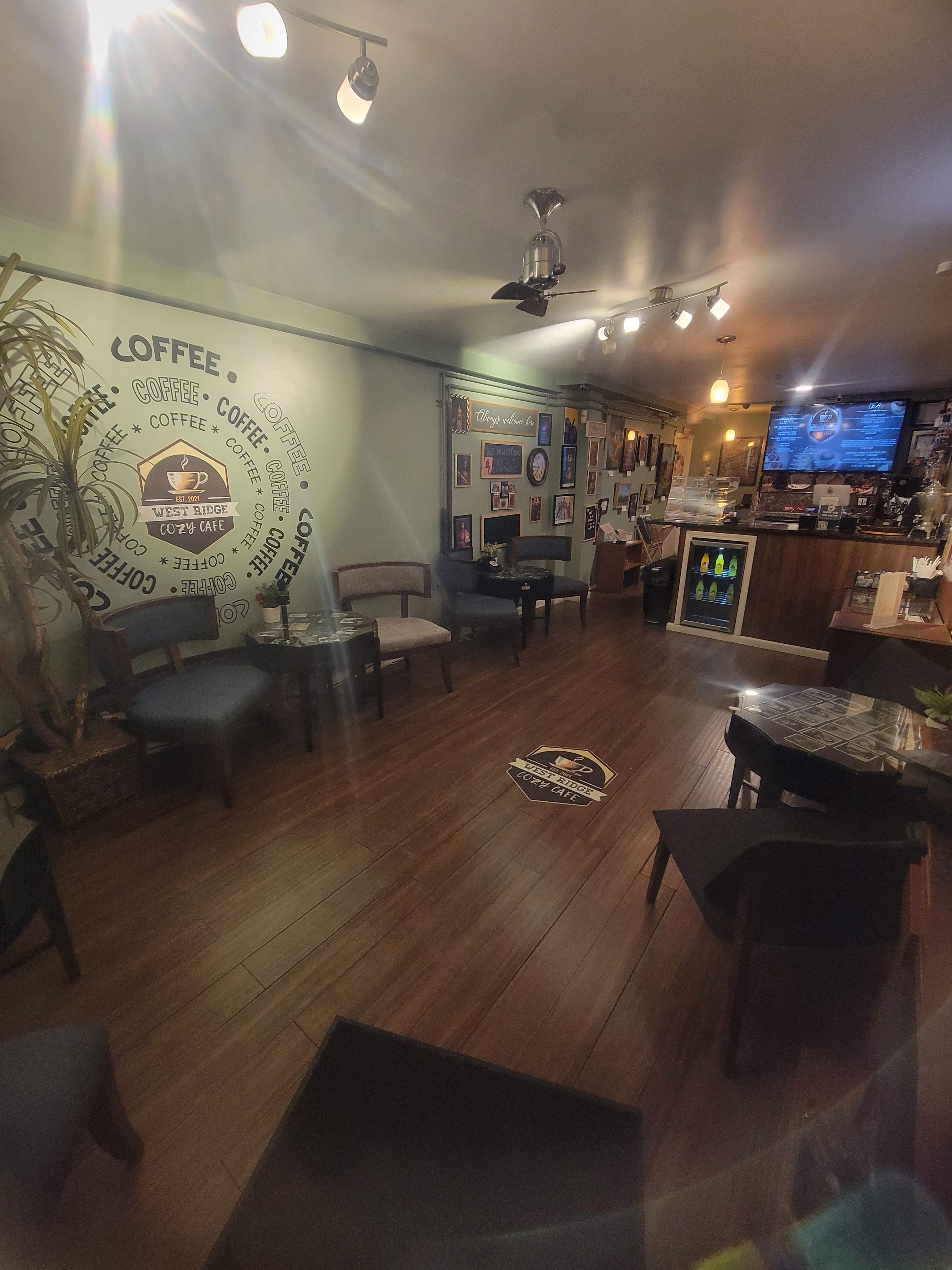 The image shows a coffee shop interior with wooden flooring, a counter displaying drinks, and walls adorned with various framed pictures.