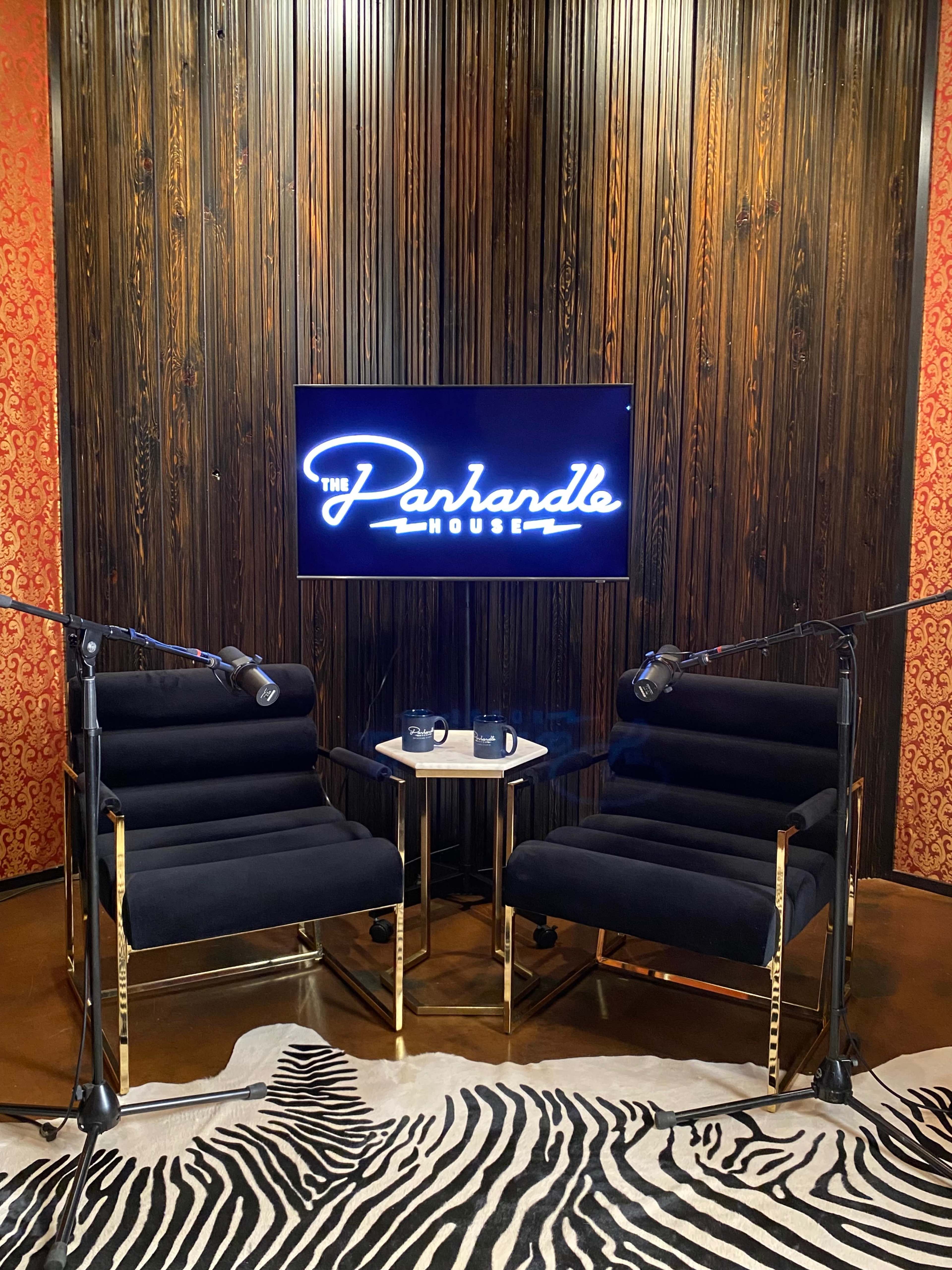 The image shows a podcast studio with two black chairs facing a small table, a television screen displaying "The Parhandle House," and microphones positioned for recording.