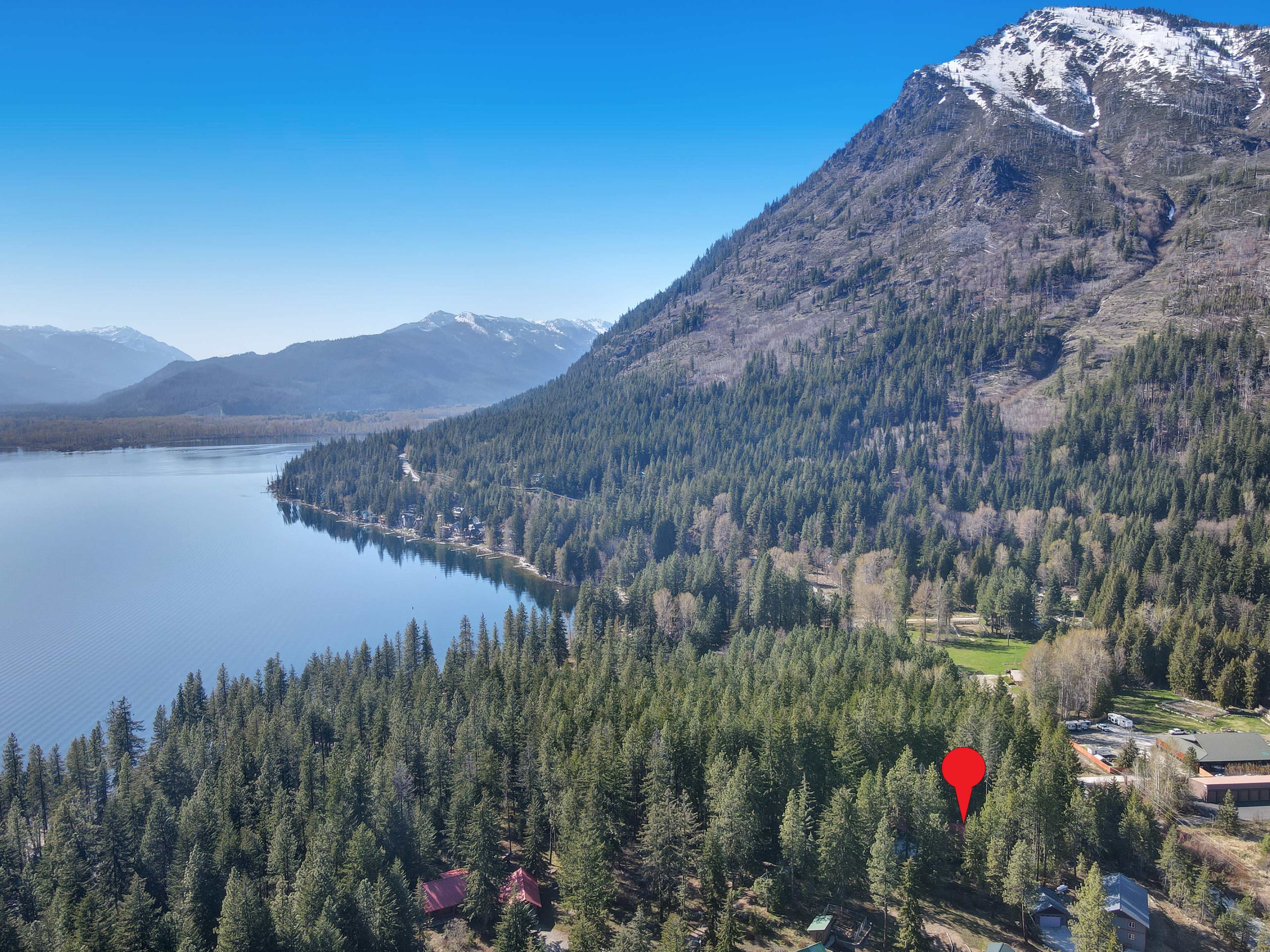 Aerial view of a mountainous landscape featuring a lake surrounded by evergreen trees and snow-capped peaks in the background.