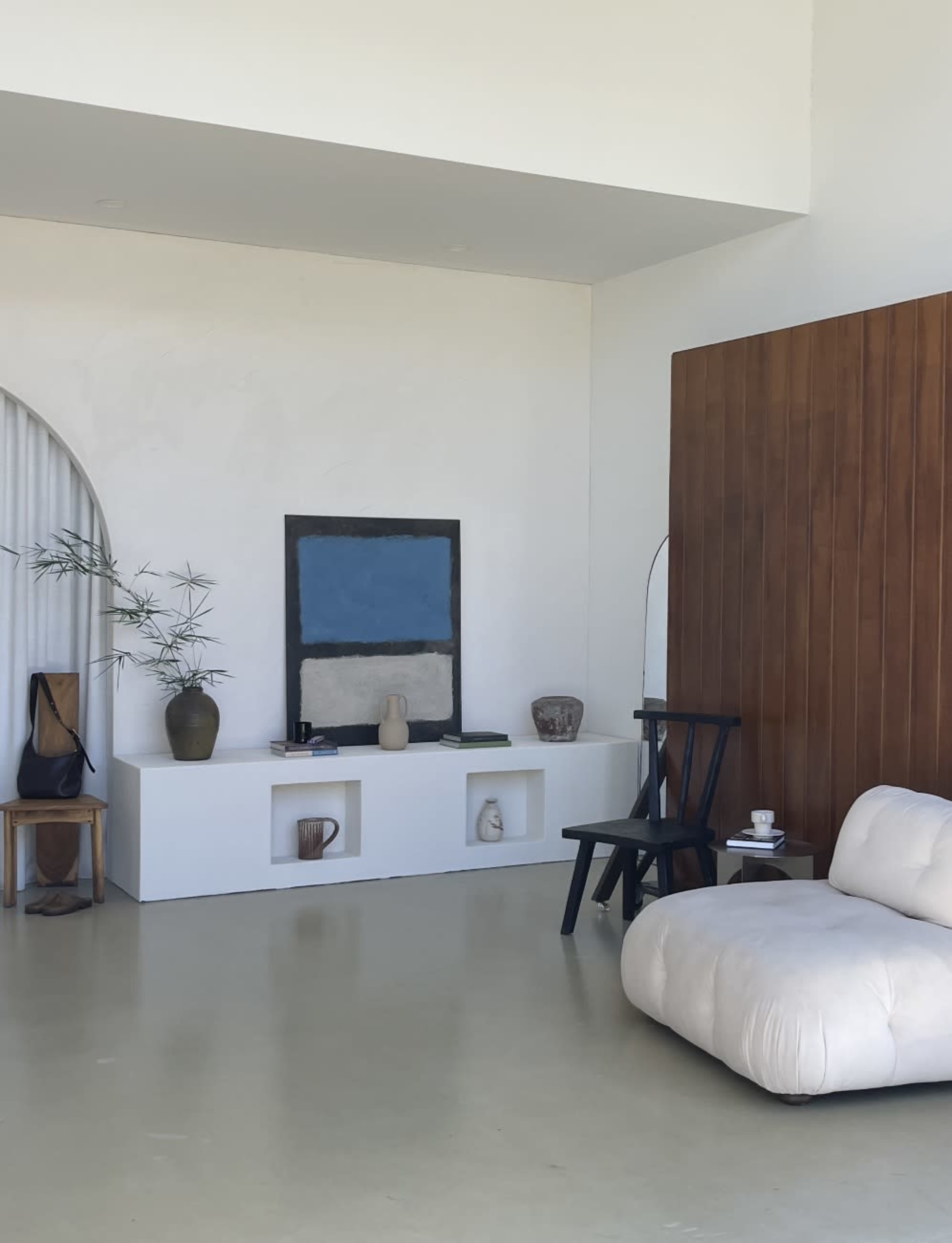 The image shows a modern interior featuring a cozy seating area with a white sofa, a wooden accent wall, and various decorative items displayed on a white shelf.