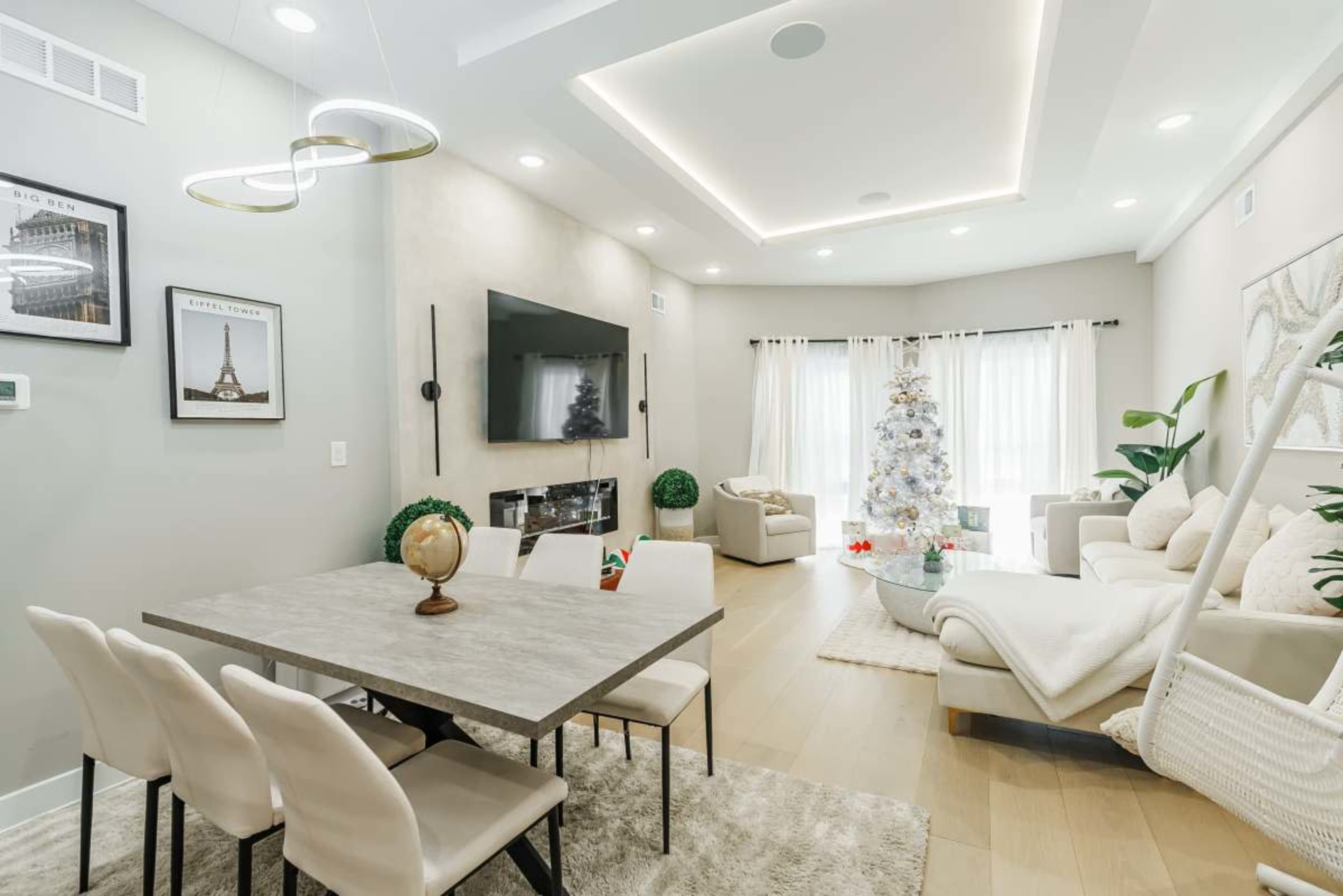 The image shows a modern living space with a dining area, a large television mounted on the wall, and a decorated Christmas tree in the corner.