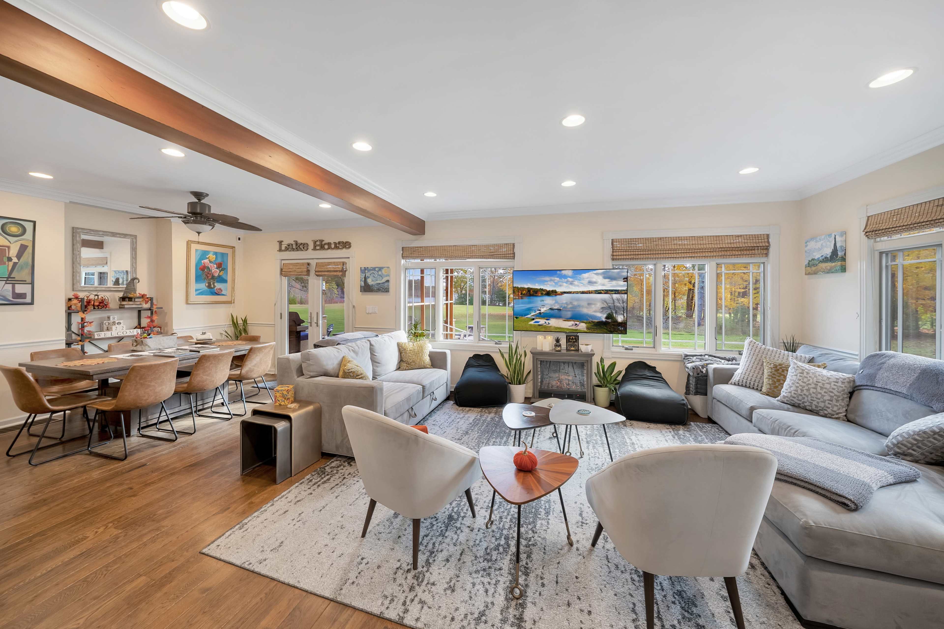 A bright, open living space featuring a large sectional sofa, a flat-screen TV, and a dining area with a wooden table and chairs.