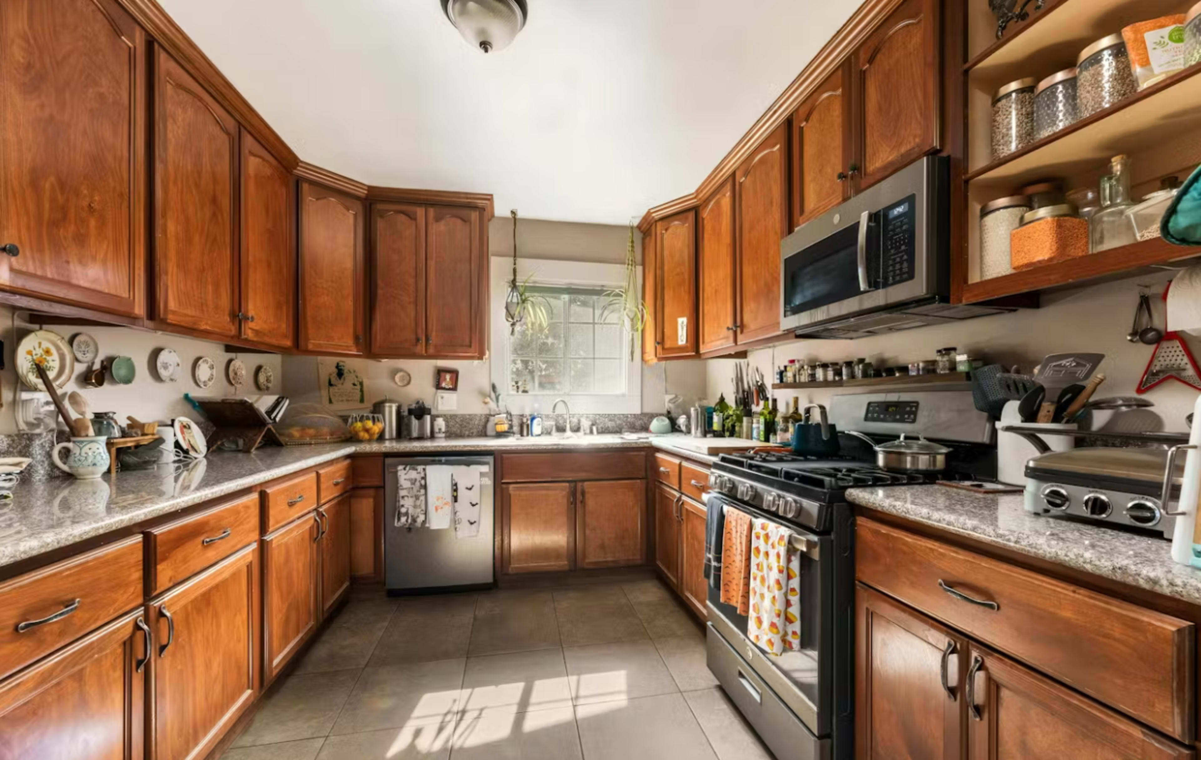 A modern kitchen features wooden cabinetry, granite countertops, stainless steel appliances, and natural light streaming through a window.