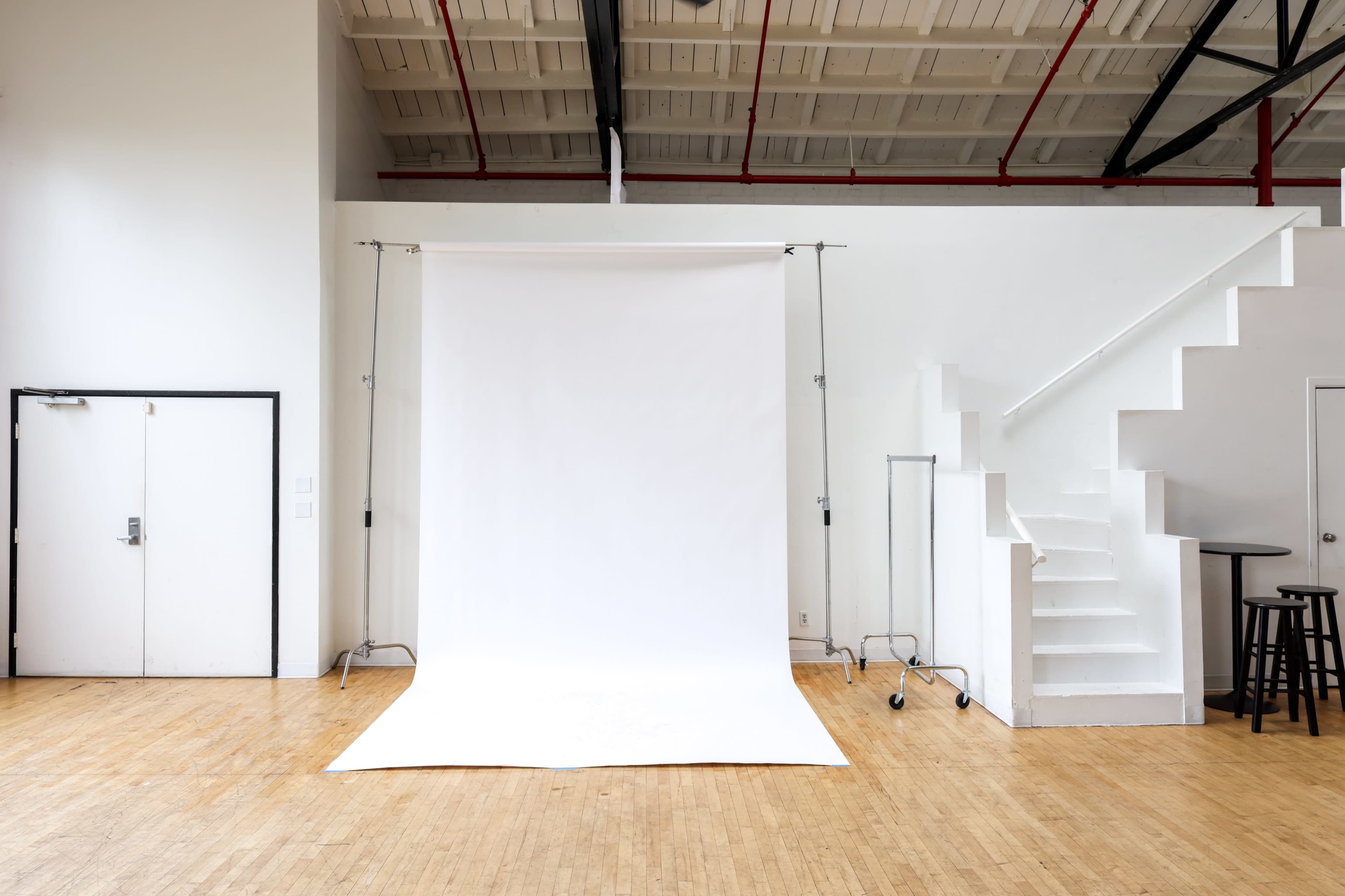 The image shows a minimalist photography studio with a white backdrop, a set of stairs, and a door on one side.