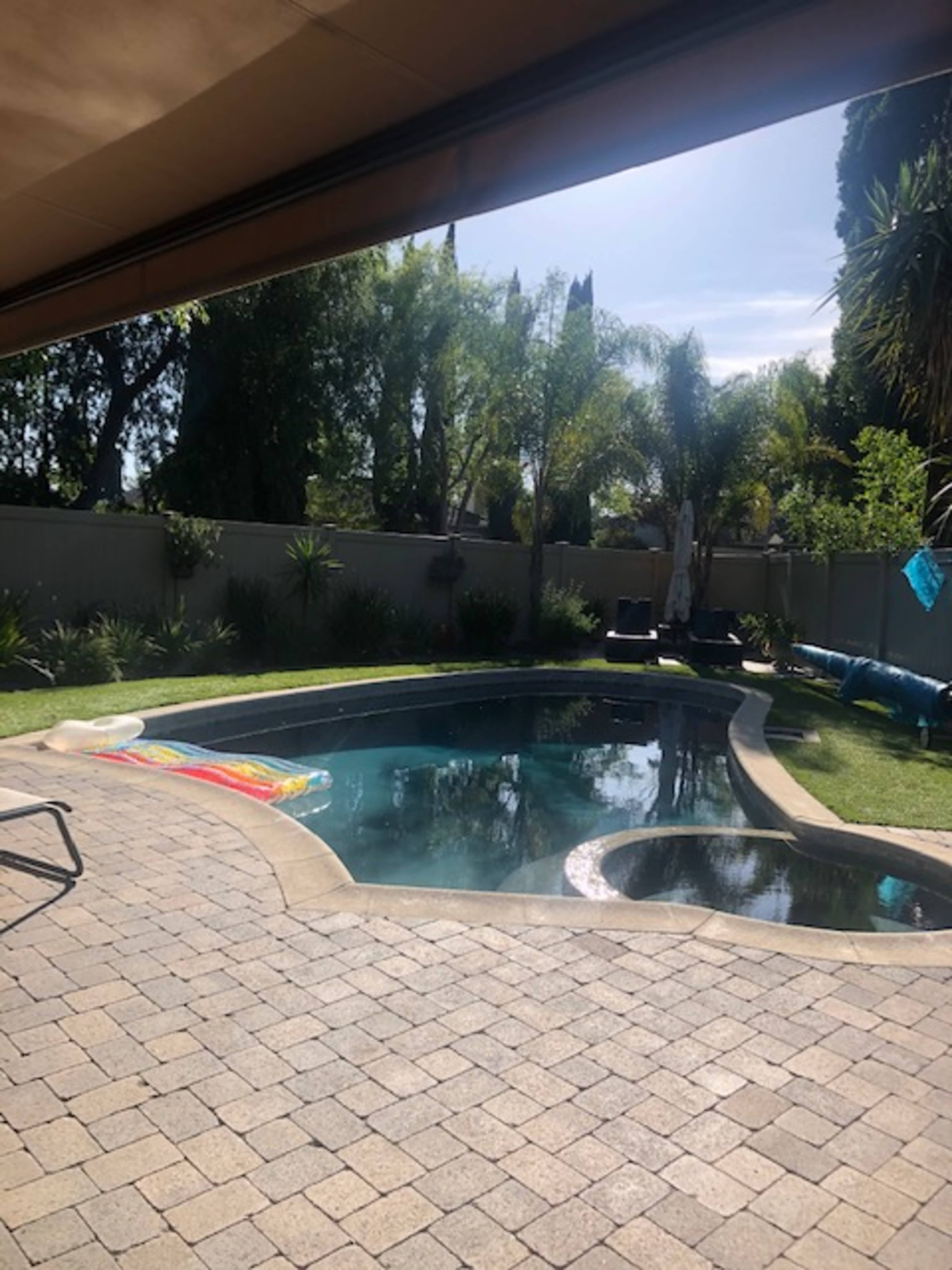 A swimming pool with a slide is surrounded by landscaped greenery and a patio area made of pavers.