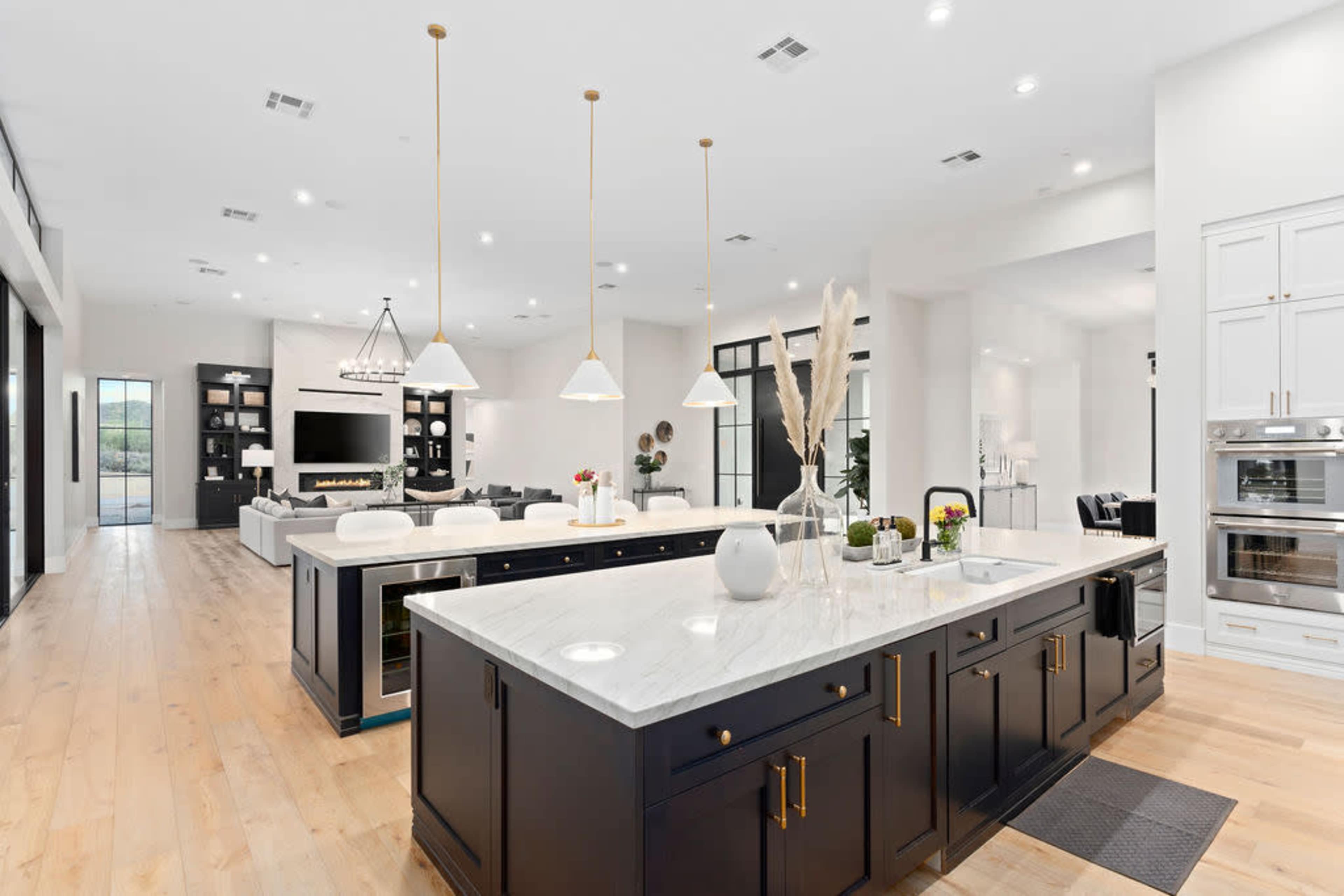 A modern kitchen with a black island, white countertops, pendant lighting, and an open layout connecting to a living area.