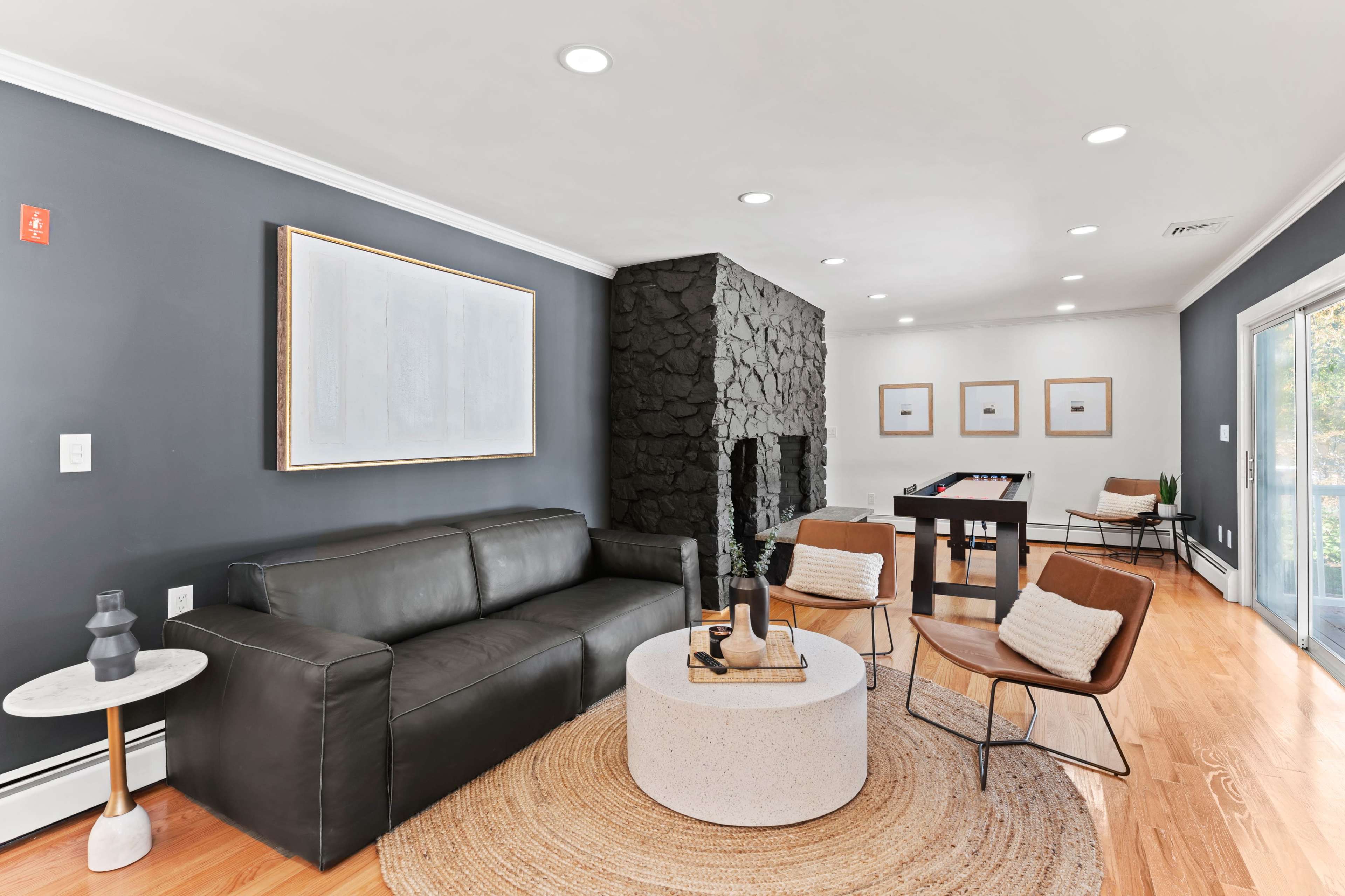 A modern living room featuring a dark sofa, a round coffee table, and a fireplace with a stone facade, complemented by a dining area in the background.