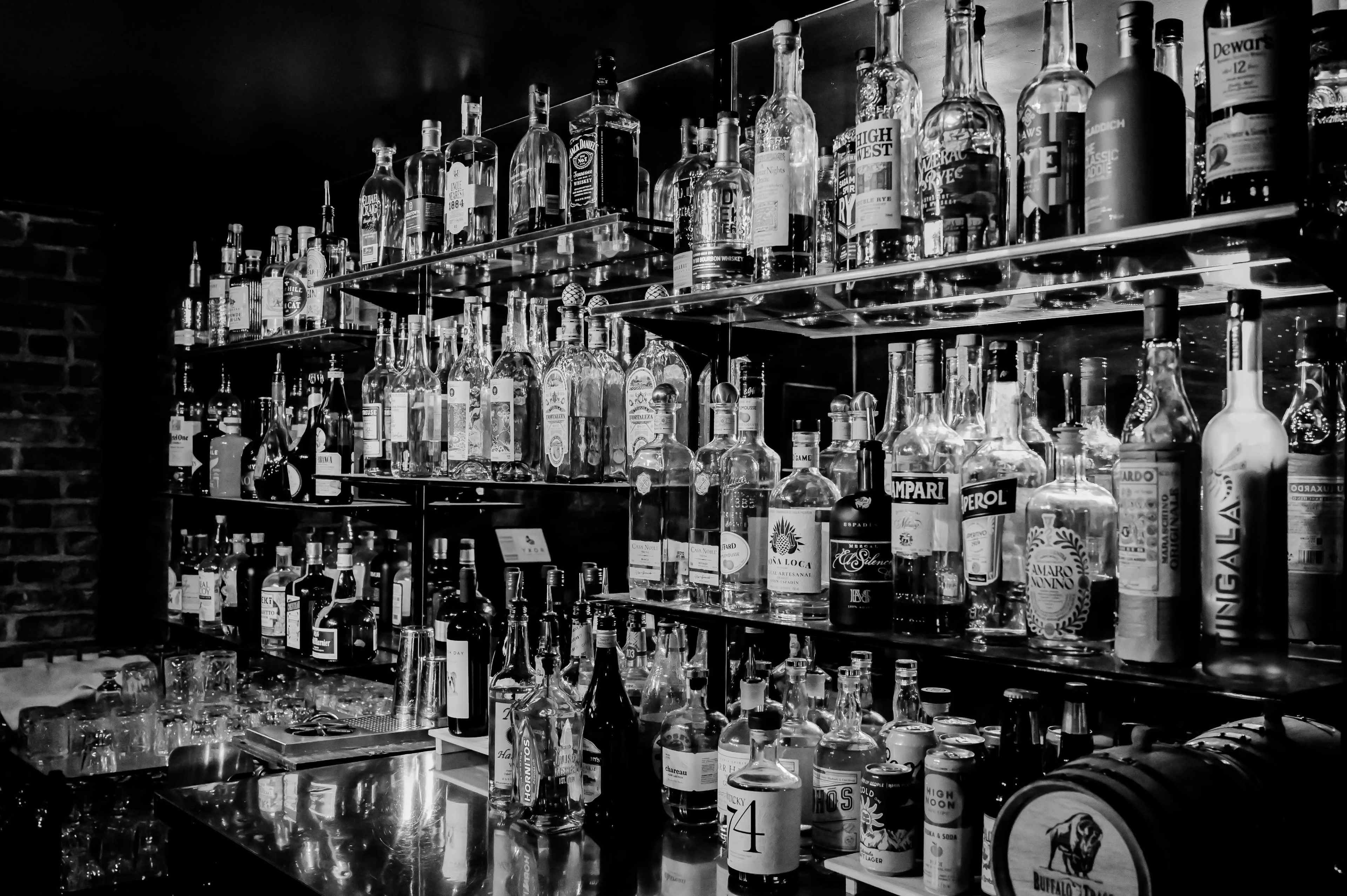 A wall of shelves displays a variety of liquor bottles in a dimly lit bar setting.