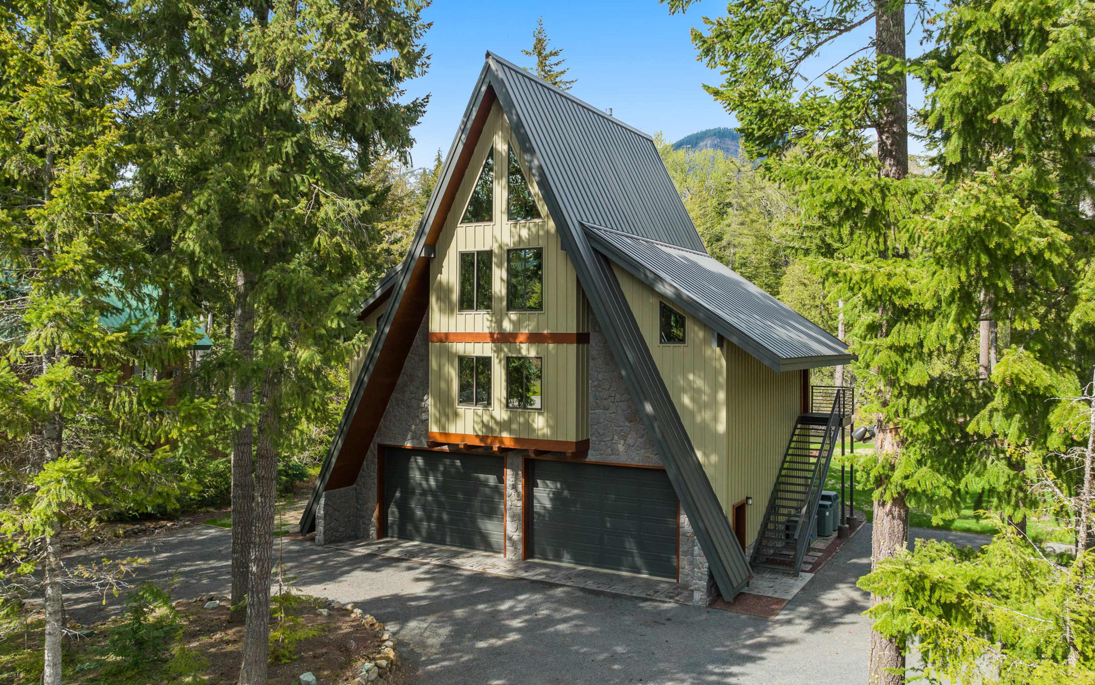 A modern A-frame house with large windows is nestled among tall pine trees.