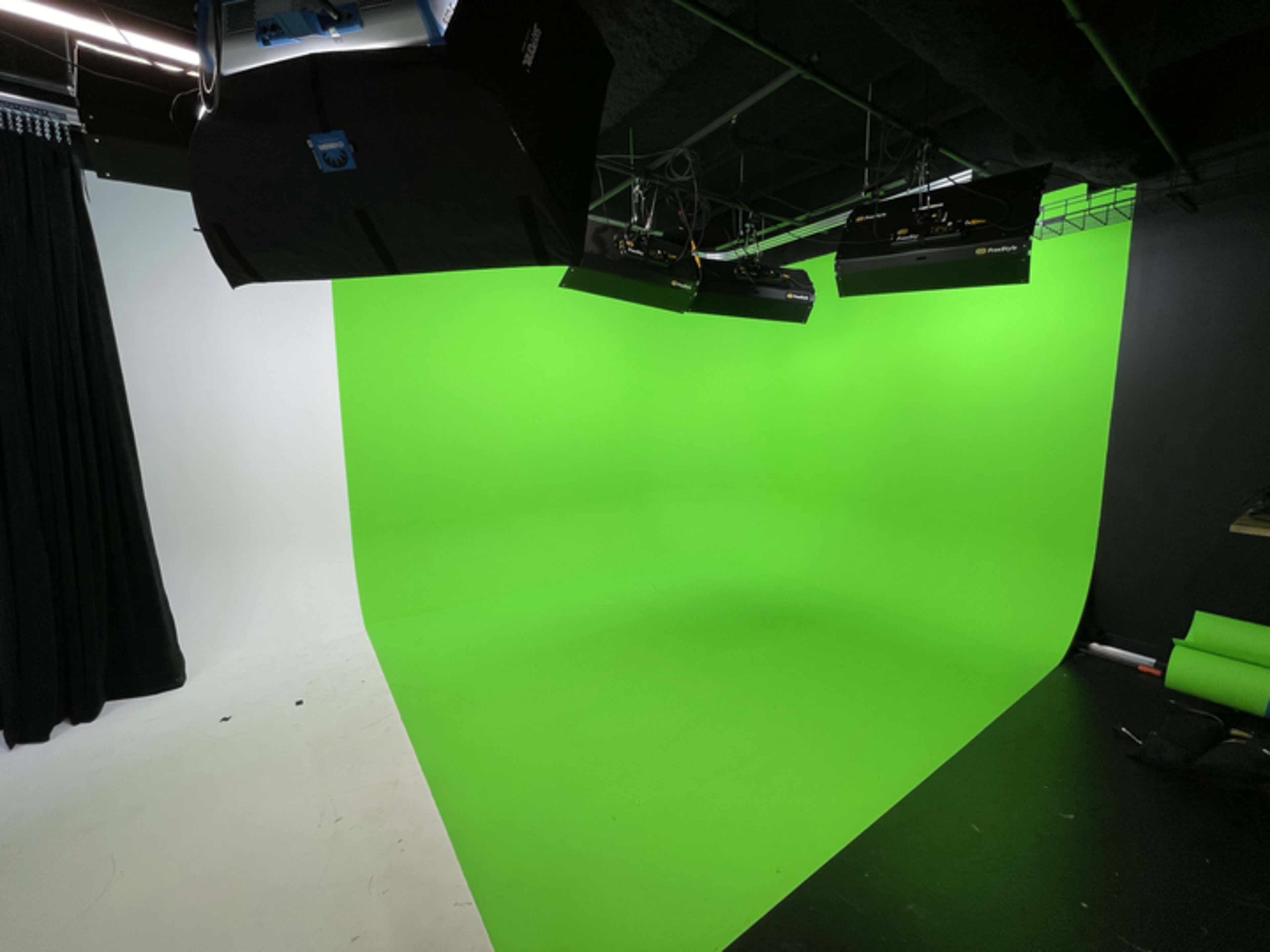 A studio space featuring a green screen background with adjustable lighting and dark curtains on one side.