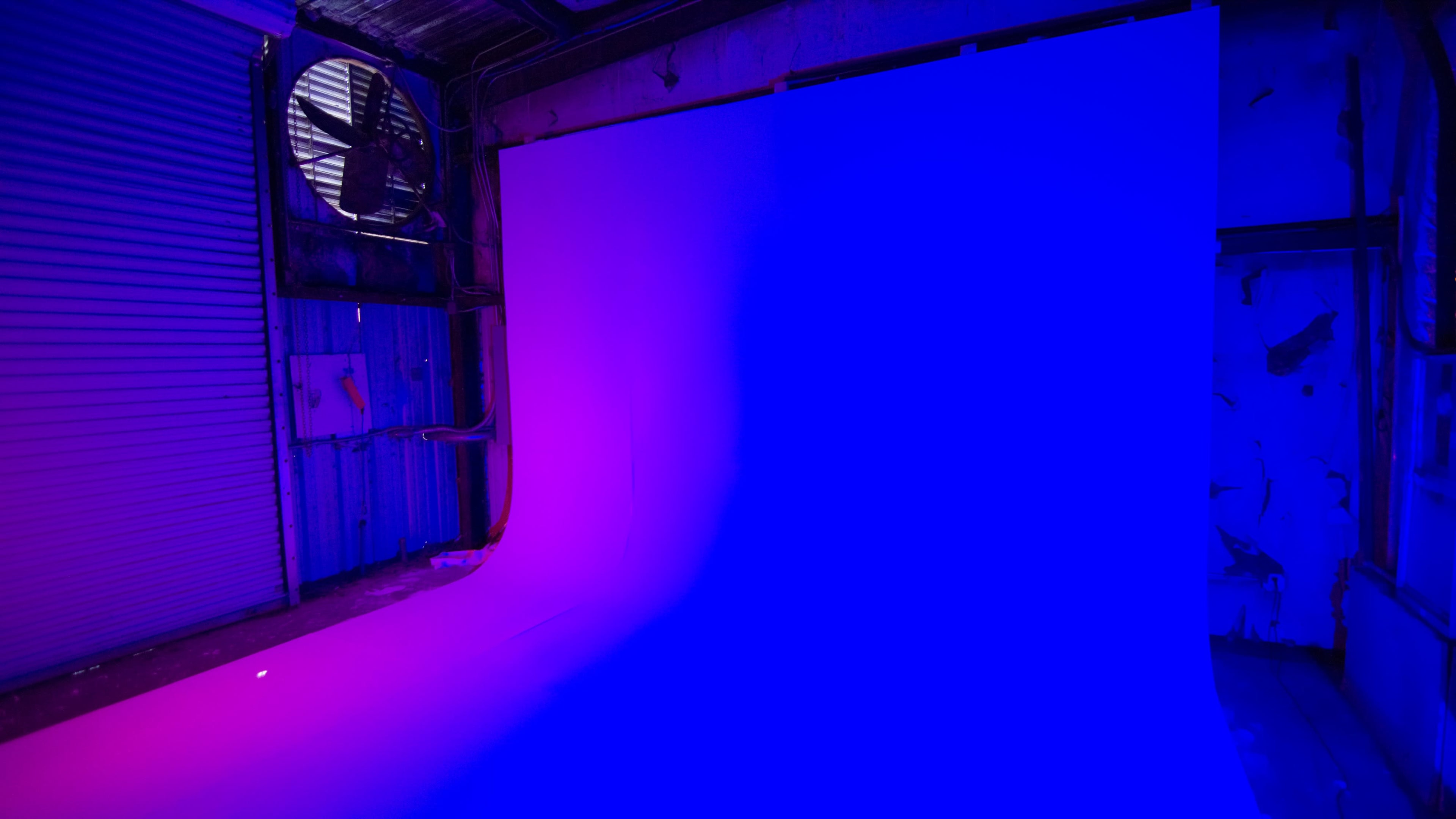 A studio backdrop displays a gradient of purple and blue hues with industrial elements in the background.