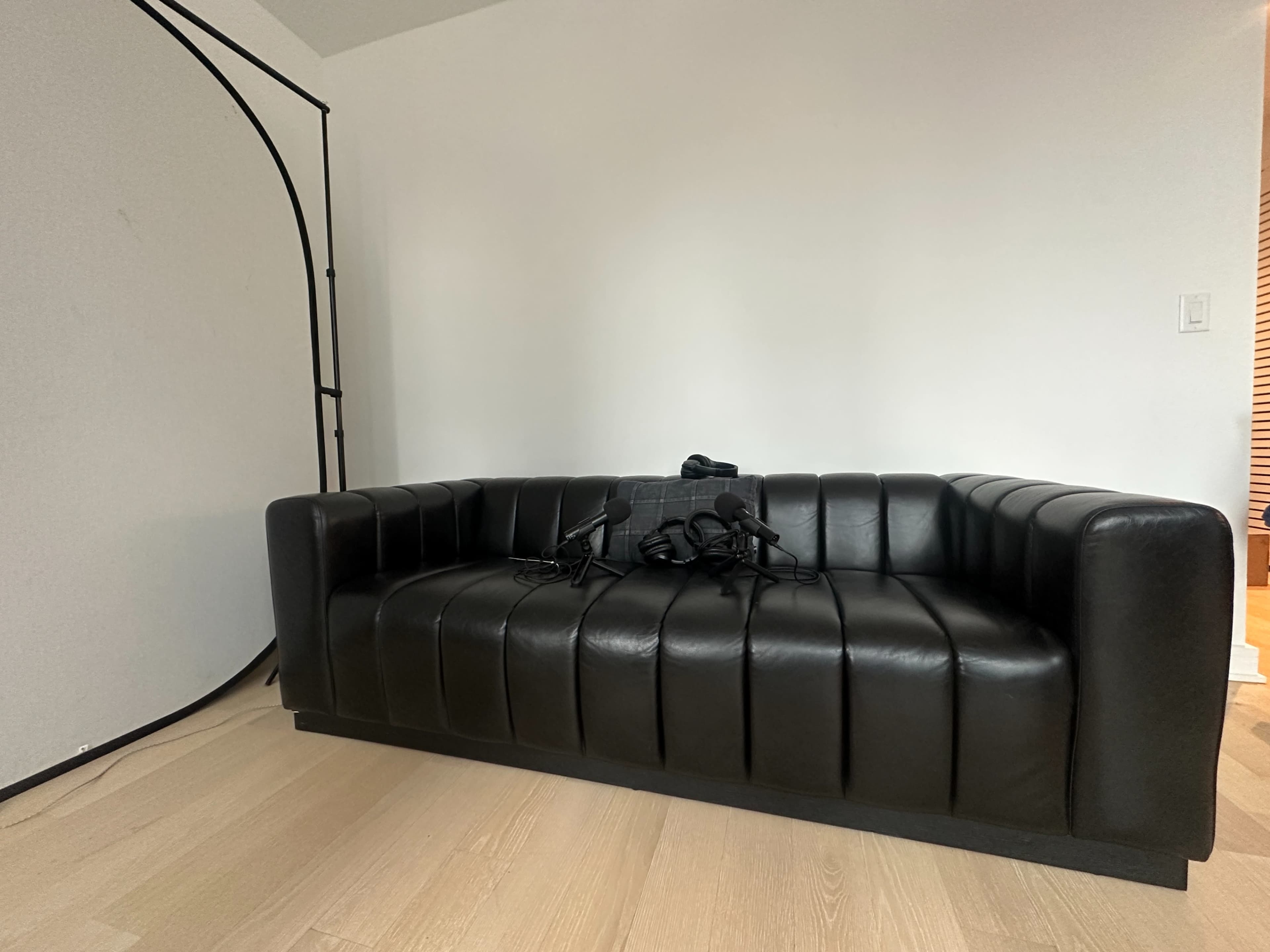 A black leather couch is positioned against a light-colored wall with a curved backdrop nearby.