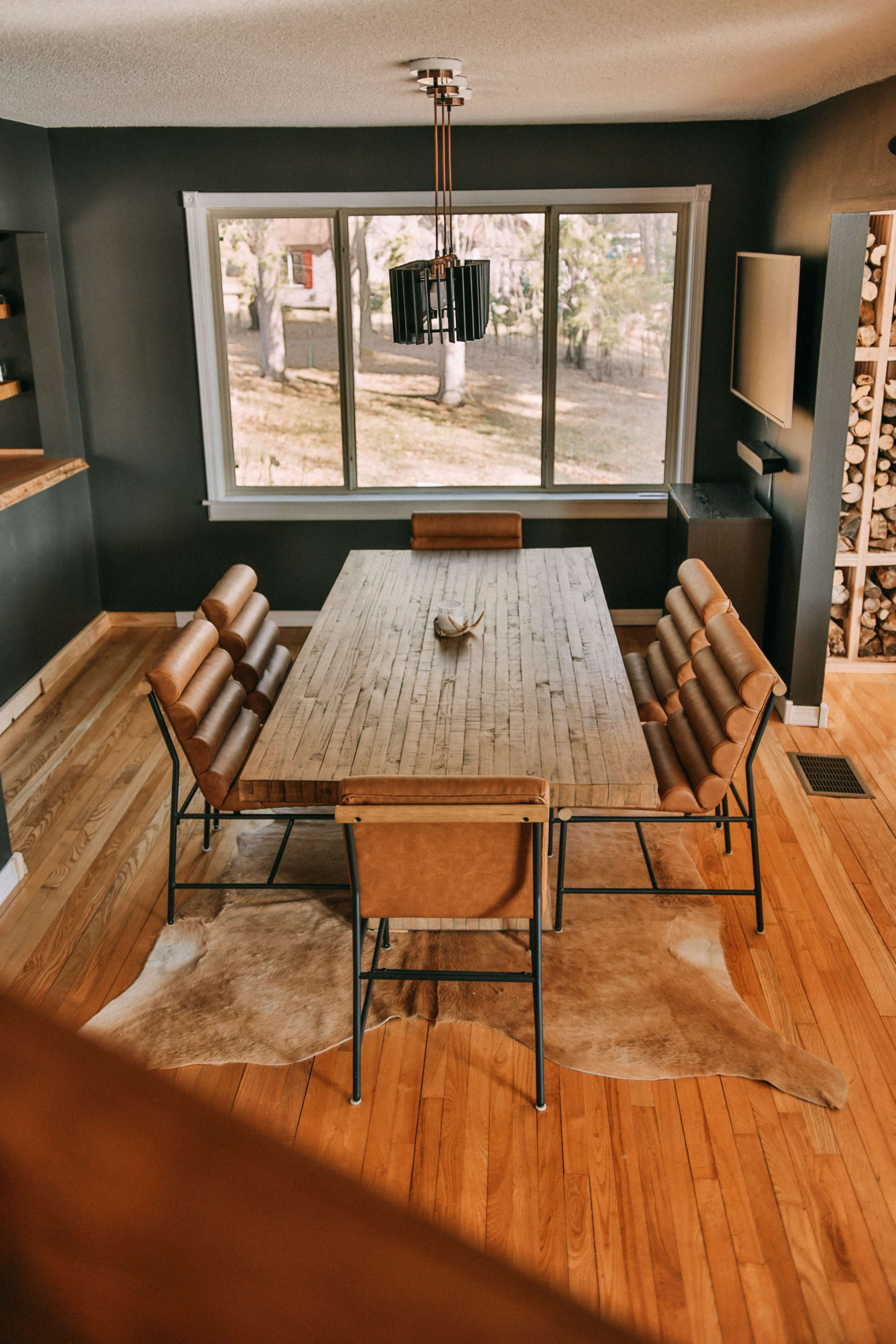 A dining area features a large wooden table surrounded by leather chairs, with a view of the outdoors through large windows.