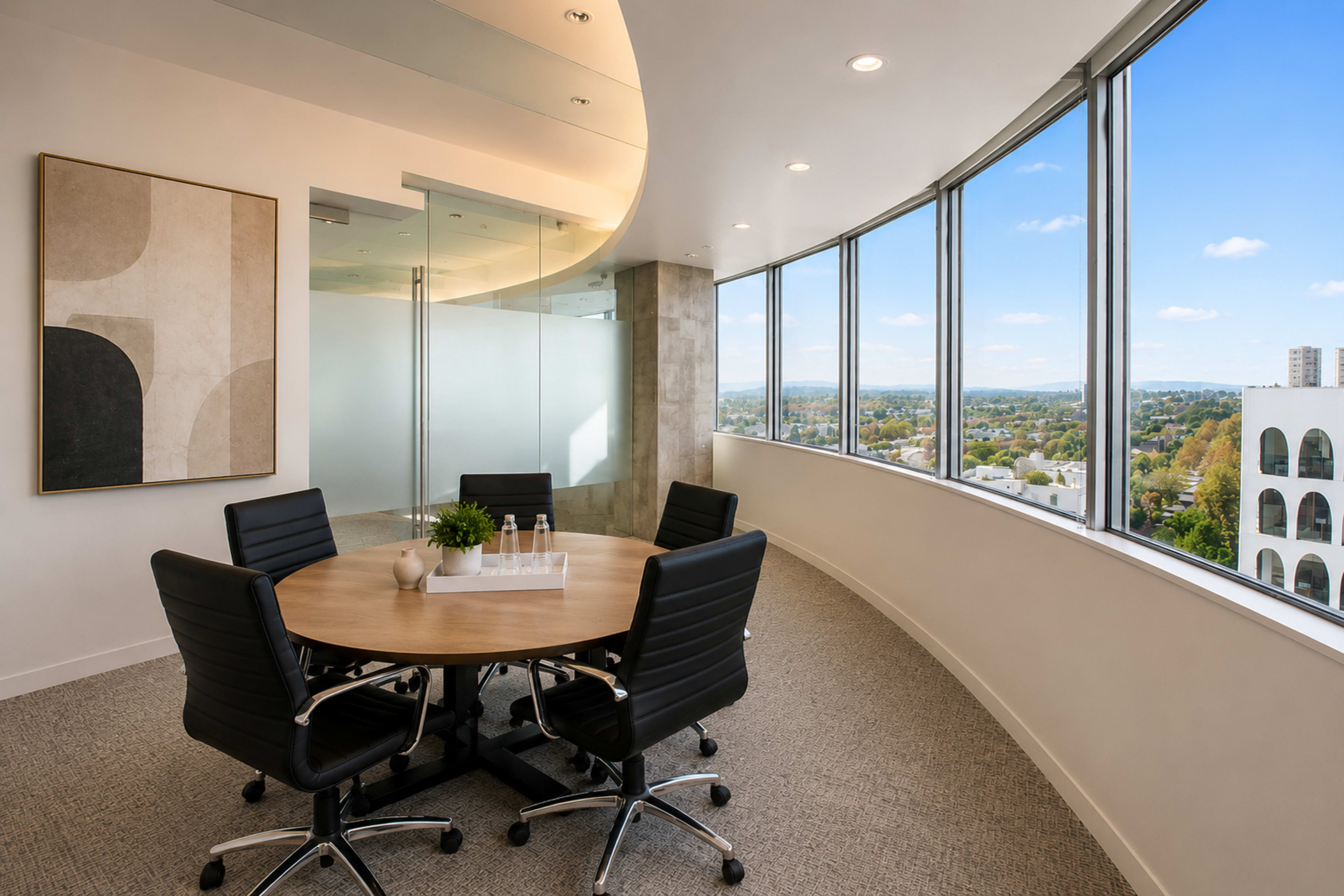 A modern conference room features a circular table surrounded by chairs and large windows offering a view of the cityscape.