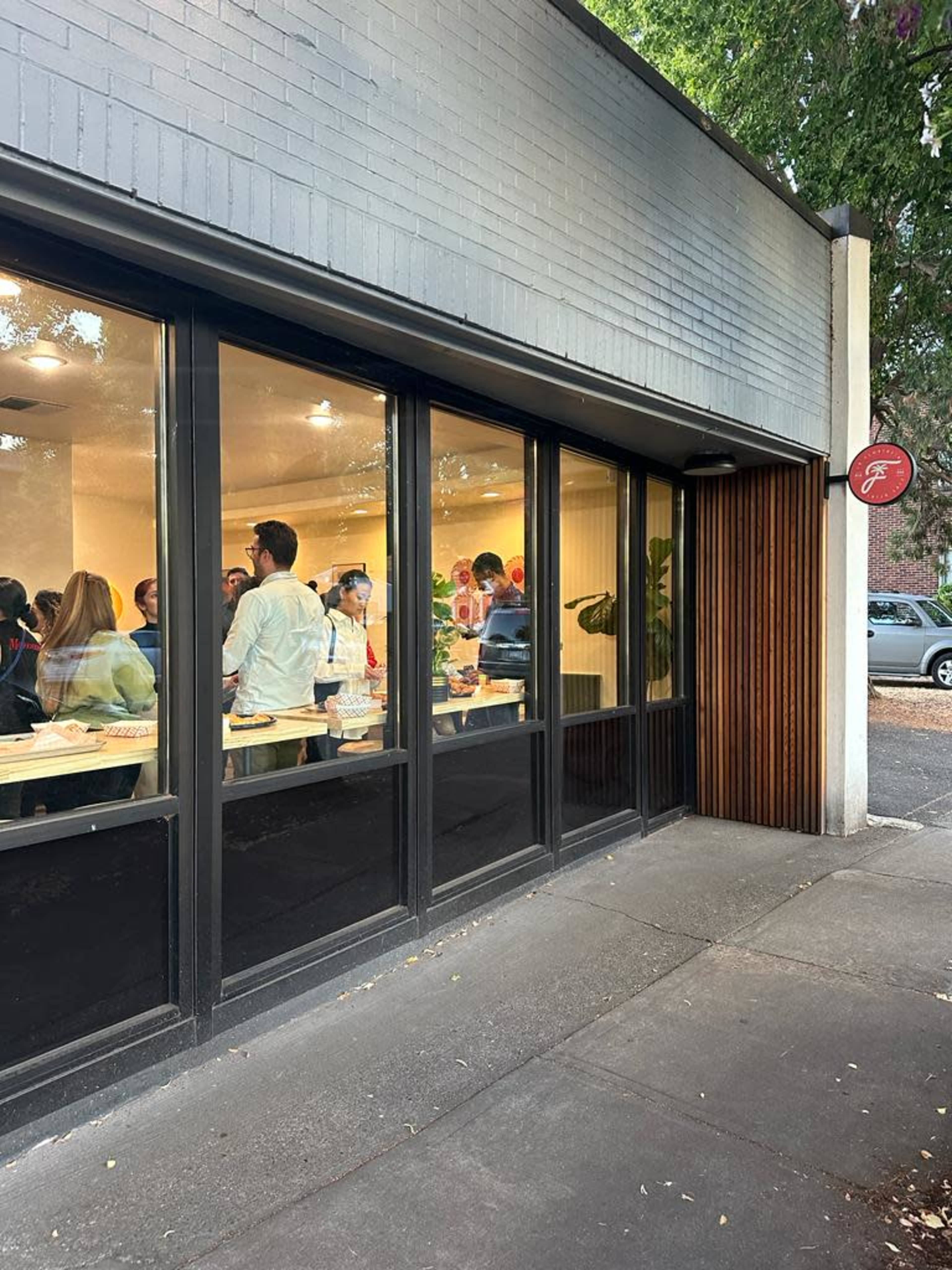 A group of people is gathered inside a modern cafe, as seen through large windows.