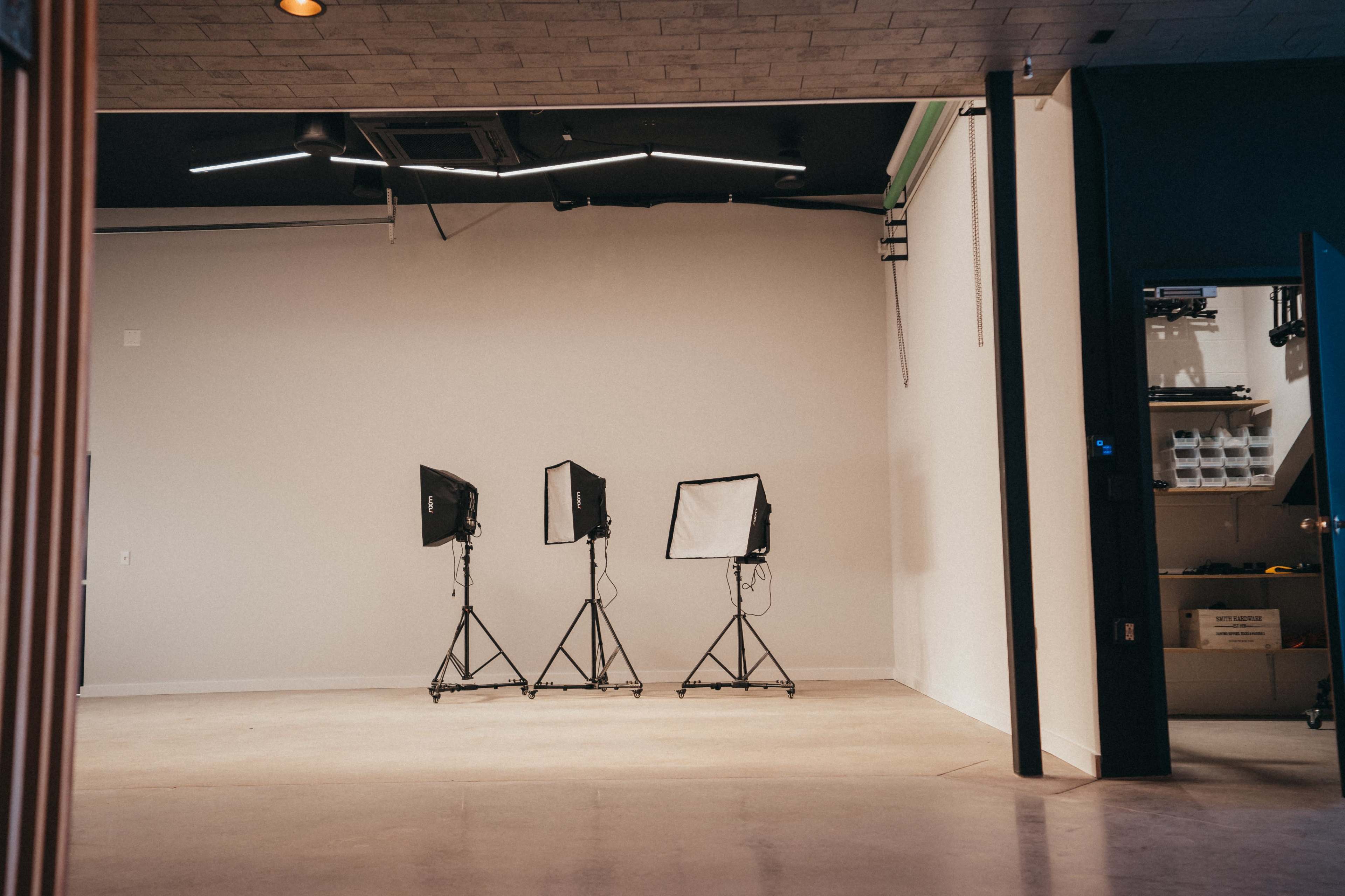 A spacious room with three positioned lighting equipment setups against a plain wall.