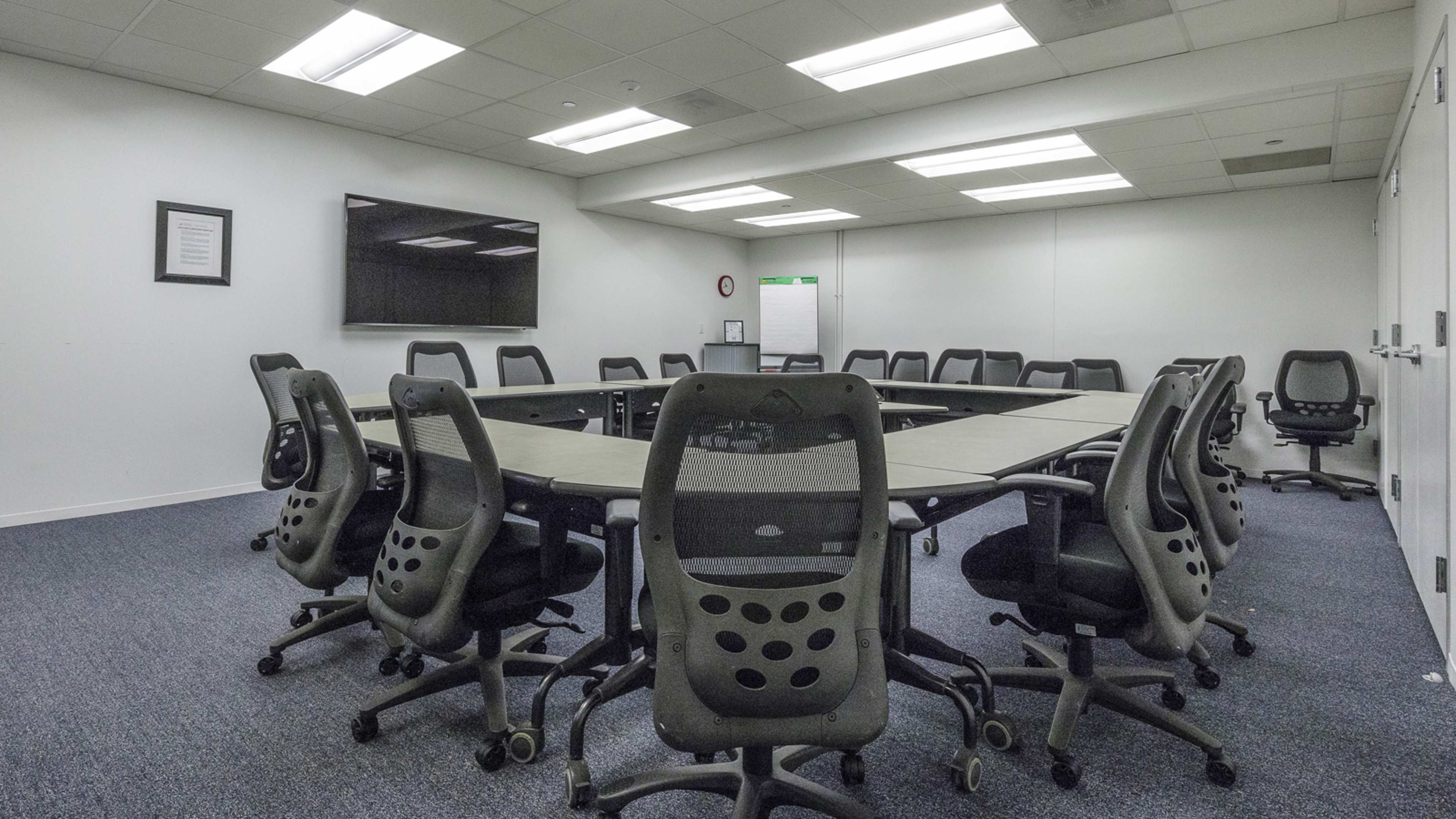 A large conference room features a rectangular table surrounded by ergonomic chairs and a wall-mounted screen.