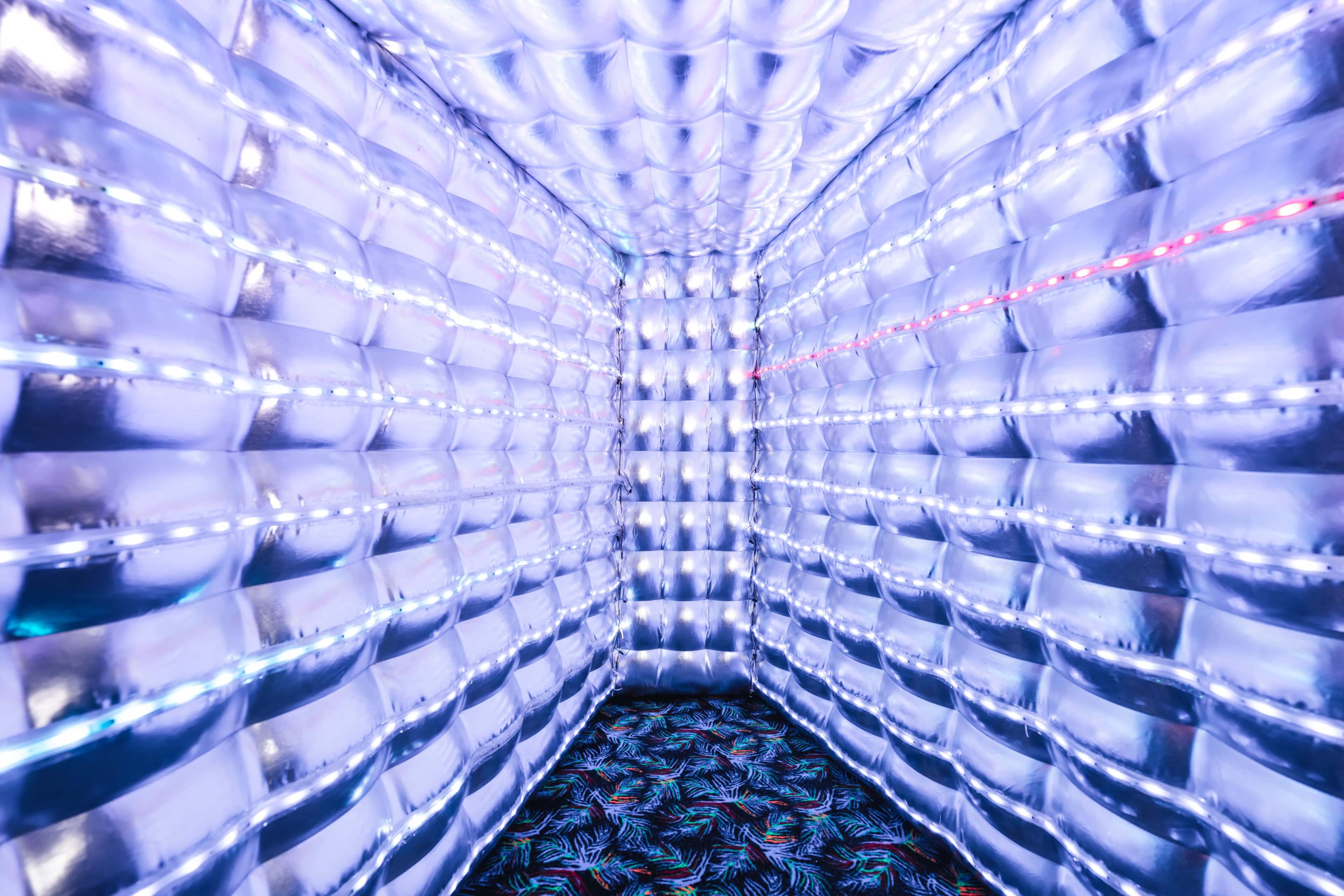 The image shows a room with metallic, reflective walls illuminated by purple lights, featuring a patterned floor.