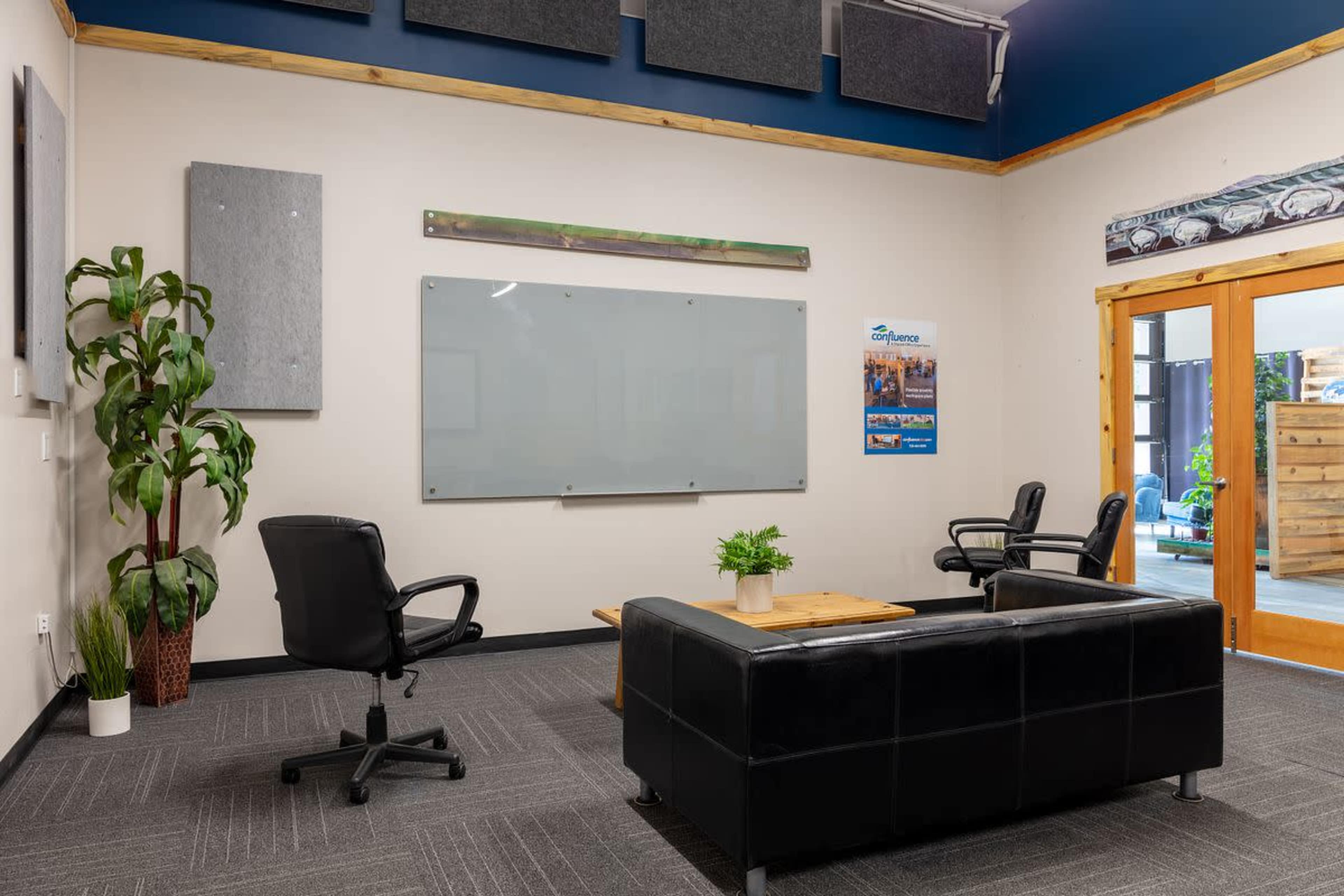 The image shows a modern meeting room with two black chairs, a wooden coffee table, a blank whiteboard, and a large glass door leading to an outdoor area.