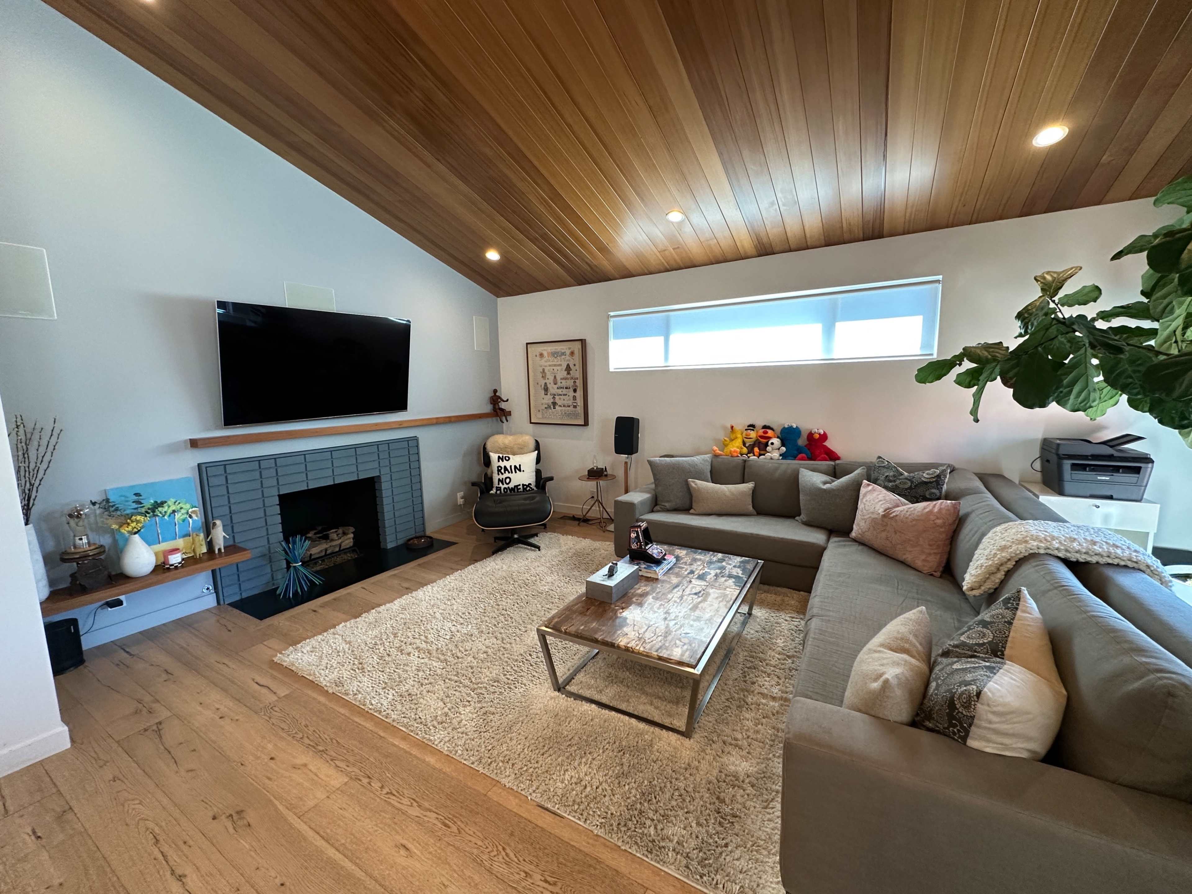 The living room features a gray sectional sofa, a wooden coffee table, a fireplace with a TV mounted above, and colorful plush toys displayed on a shelf.