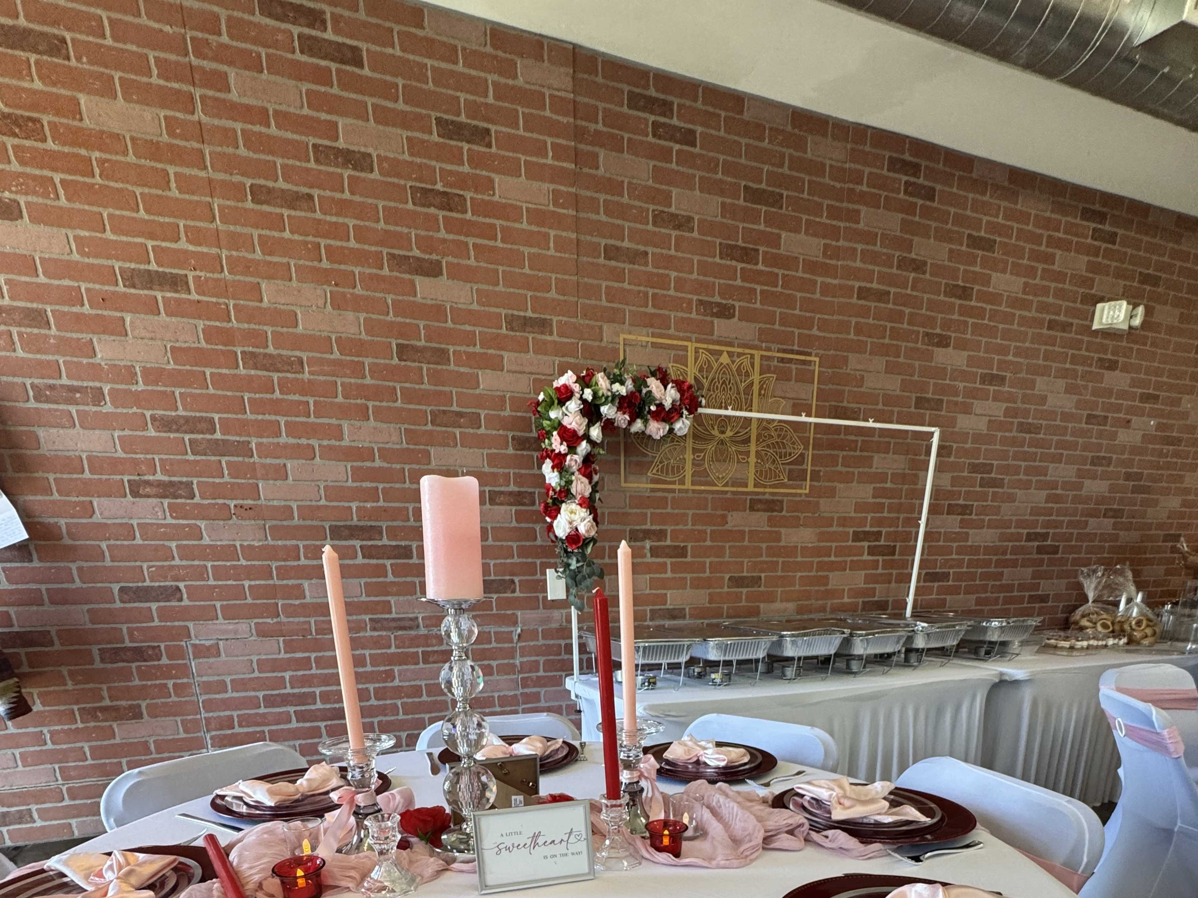 The image shows a decorated dining table with plates, candles, a floral centerpiece, and a brick wall in the background.