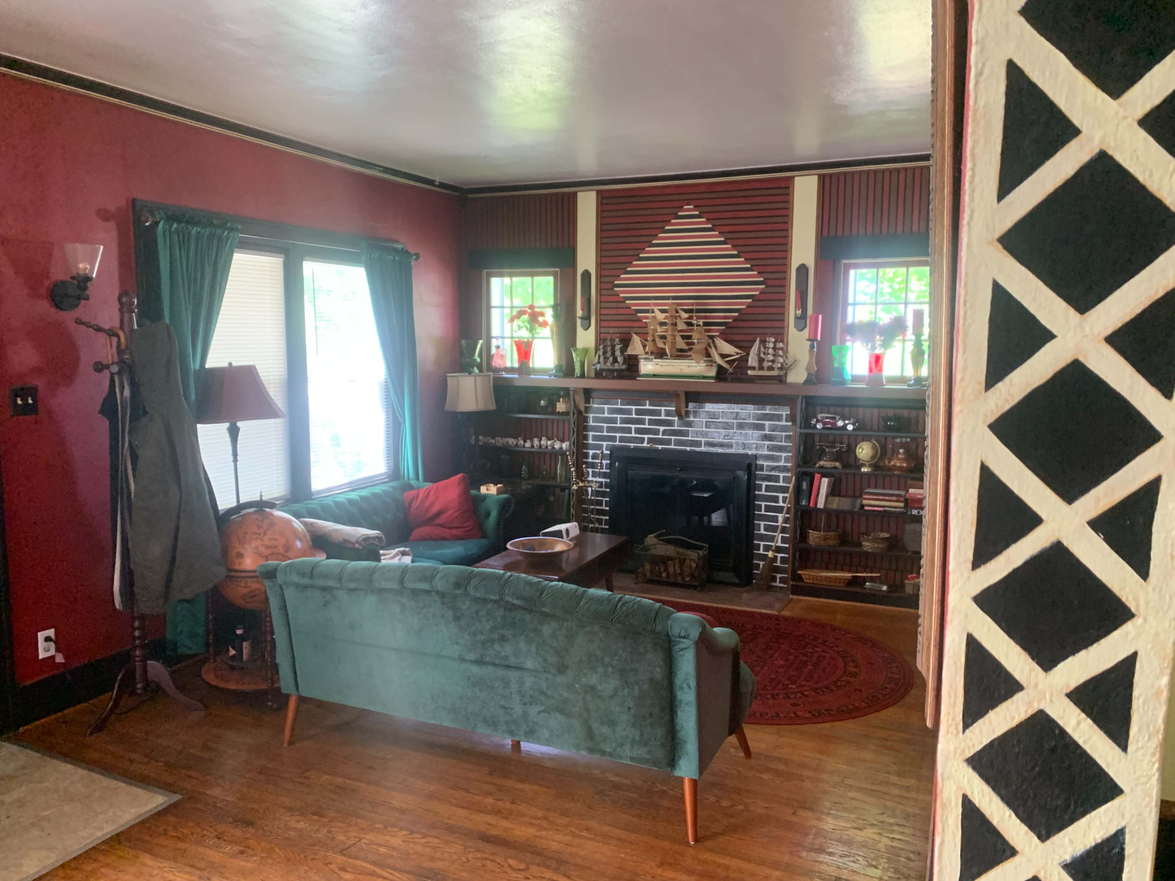 The living room features a green couch, a red accent wall, and a fireplace adorned with decorative ship models and colorful glassware.