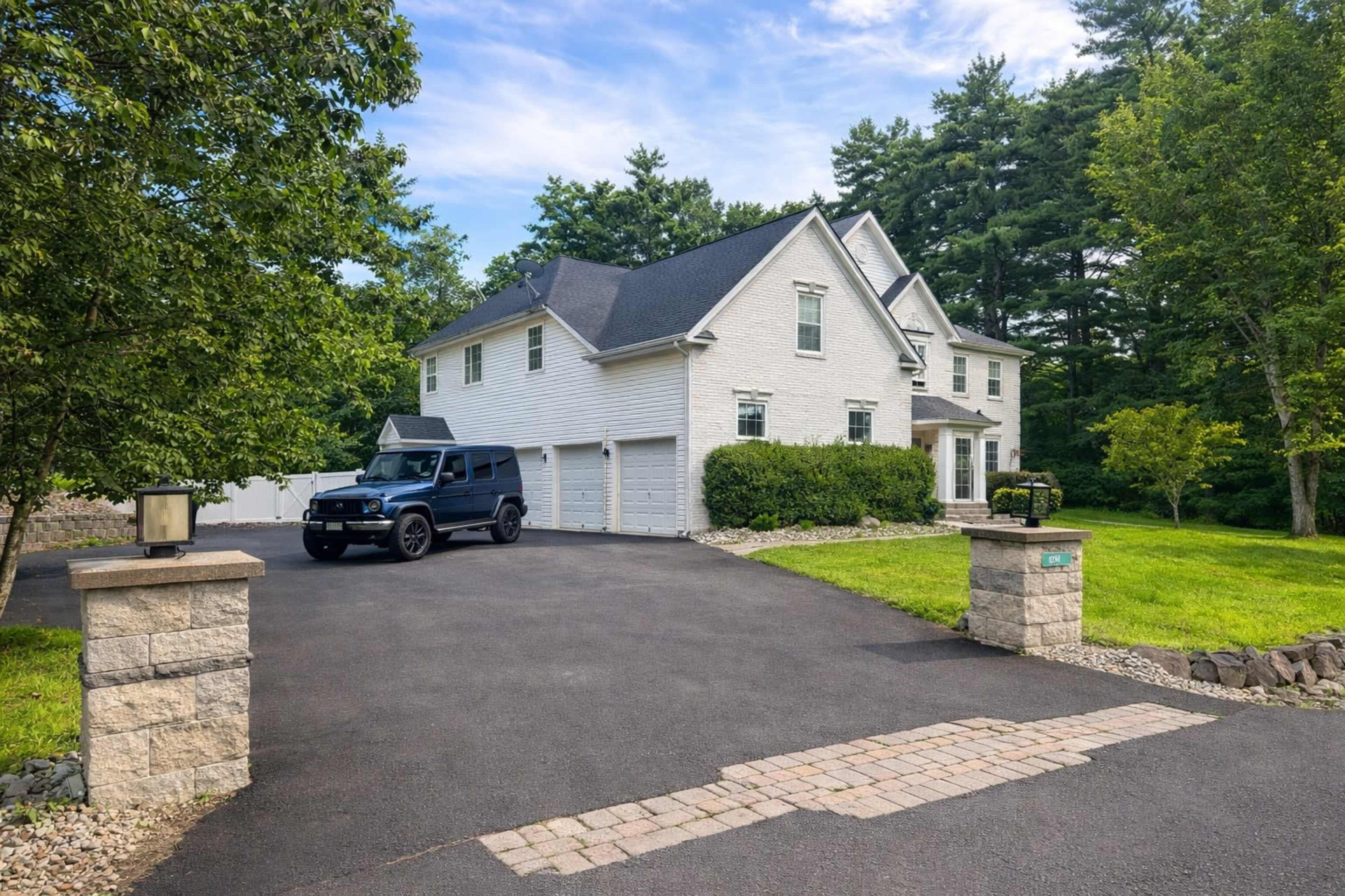A large, two-story white house with a black SUV parked in the driveway is surrounded by trees and a grassy lawn.