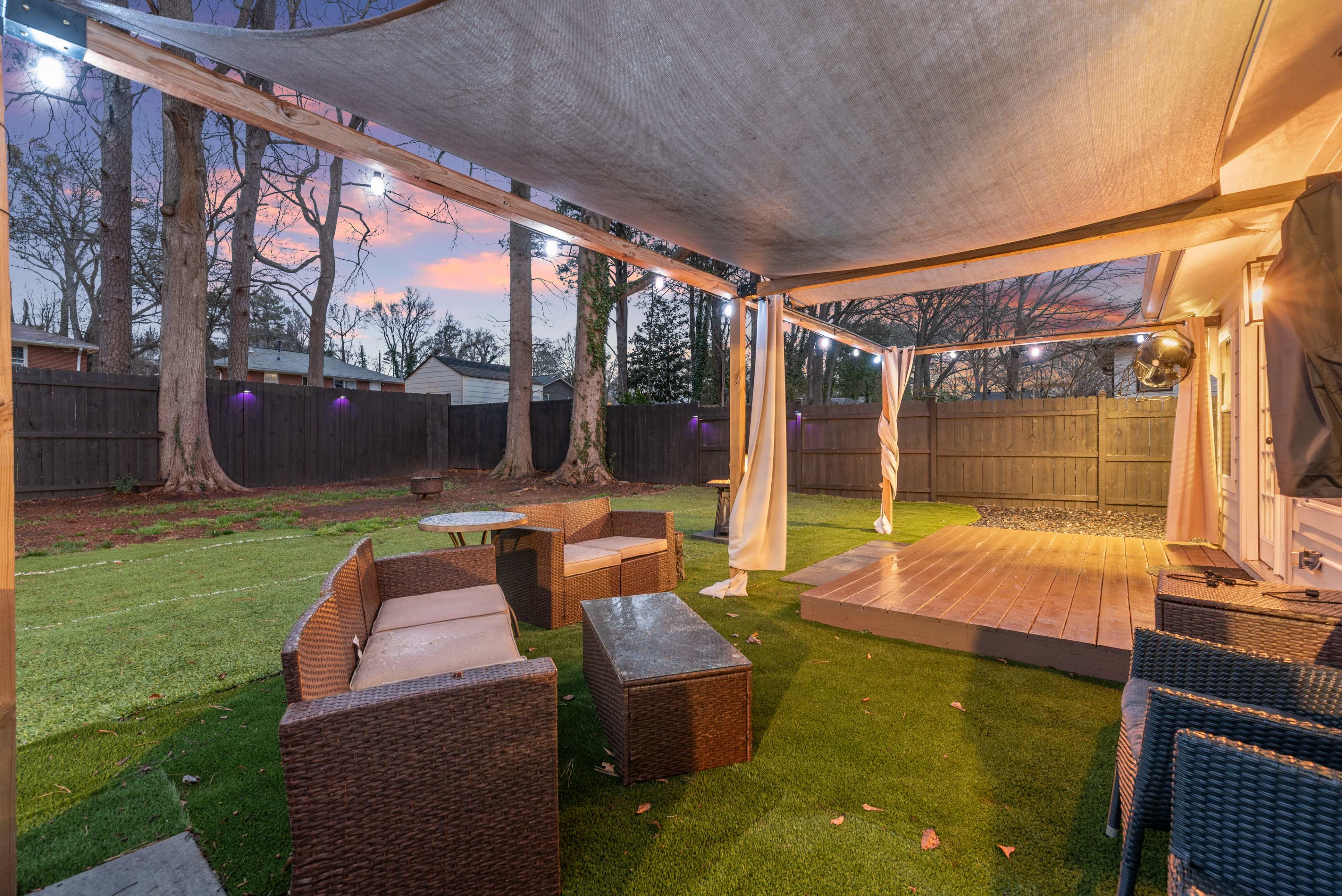 The image shows a backyard scene with outdoor seating, a wooden deck, and a grassy area under a partially illuminated sky at dusk.