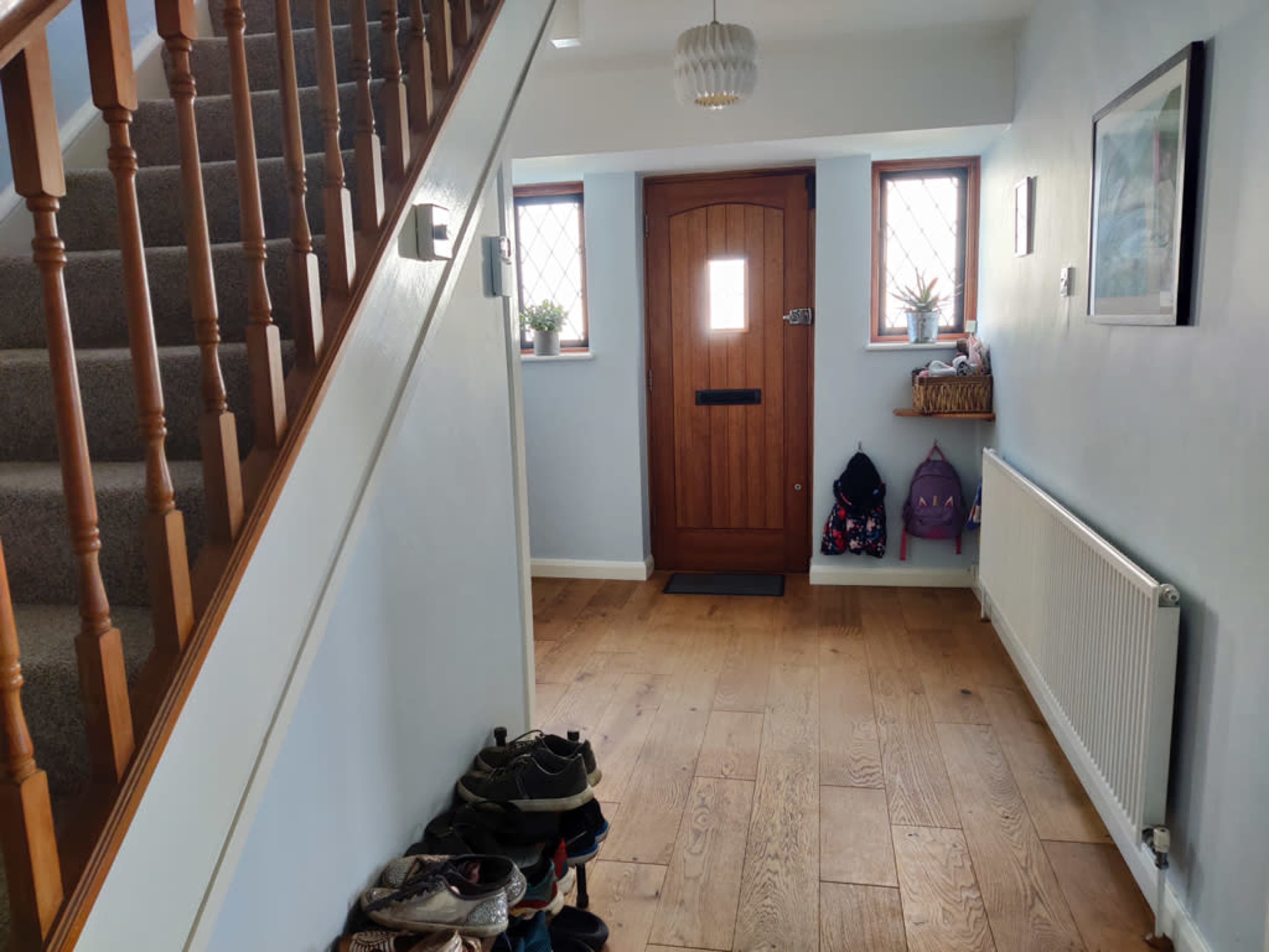 A well-lit entryway with a wooden door, a staircase on the left, and shoes neatly arranged on the floor.