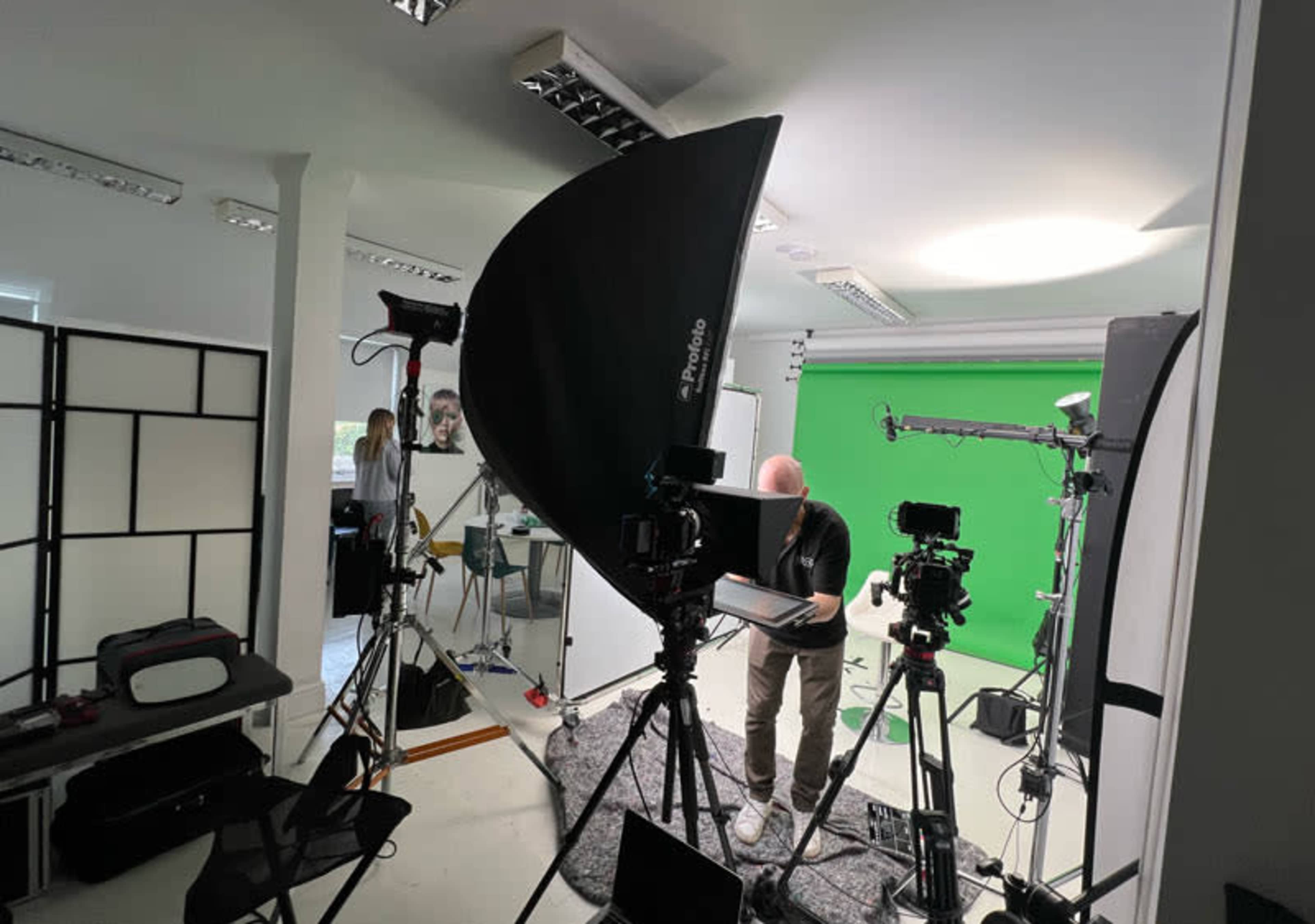 A well-equipped video production studio features a green screen, multiple cameras, lighting setups, and a crew member preparing equipment.
