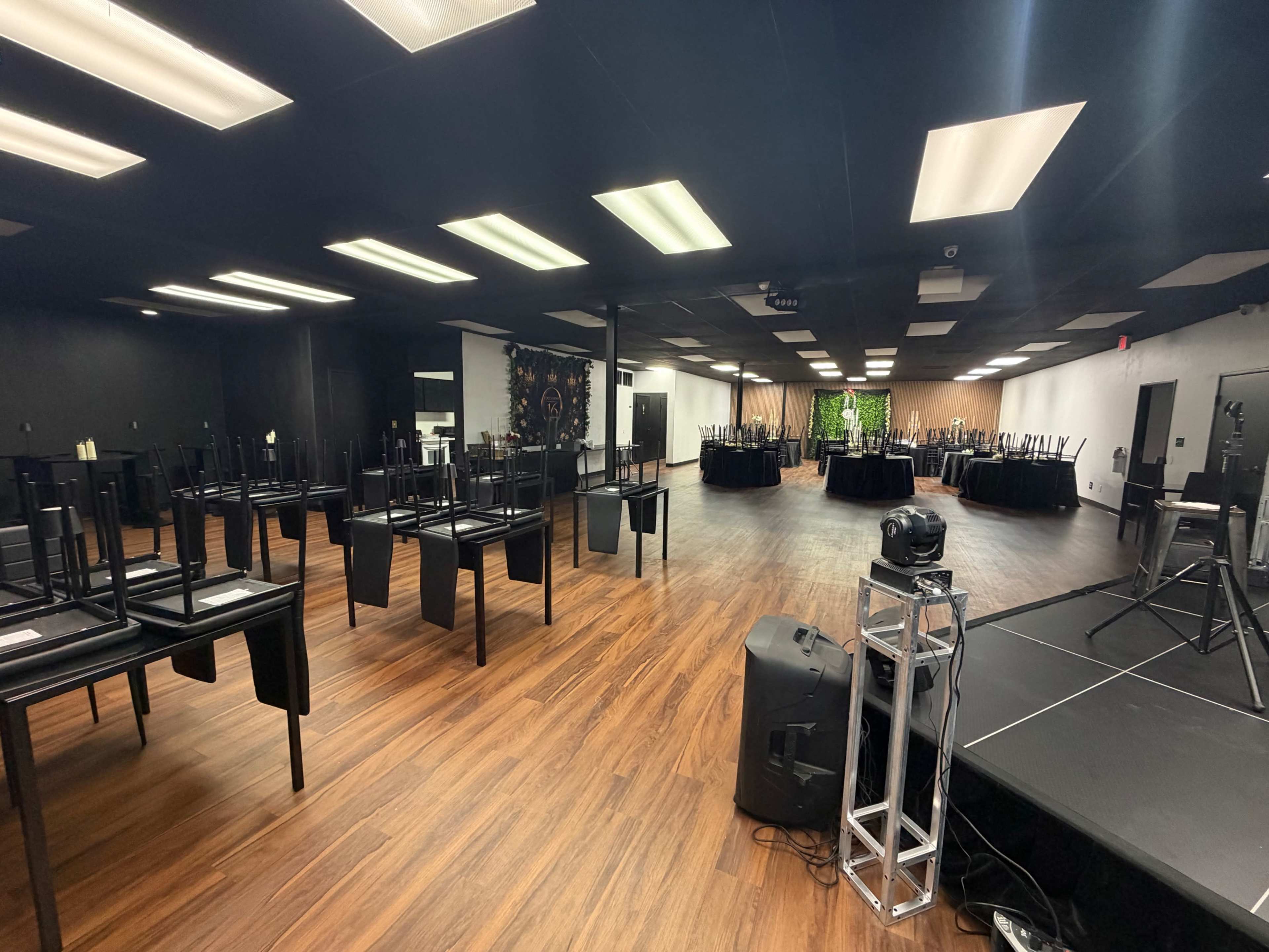 The image shows a large event space with black chairs stacked on tables and several round tables set up around the room.