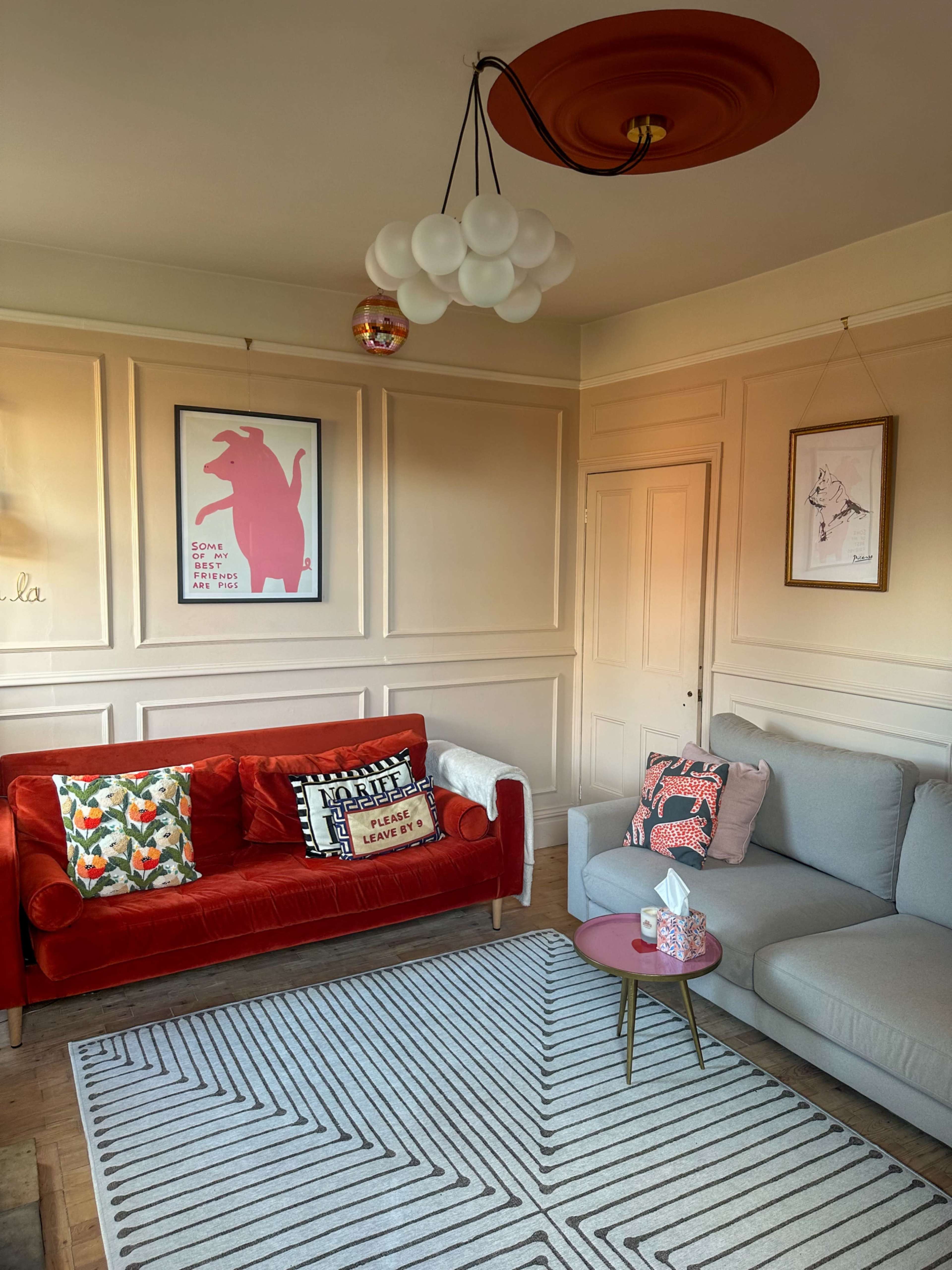 A living room with a red velvet sofa and a gray sectional, framed artwork on the walls, and a geometric rug on the wooden floor.