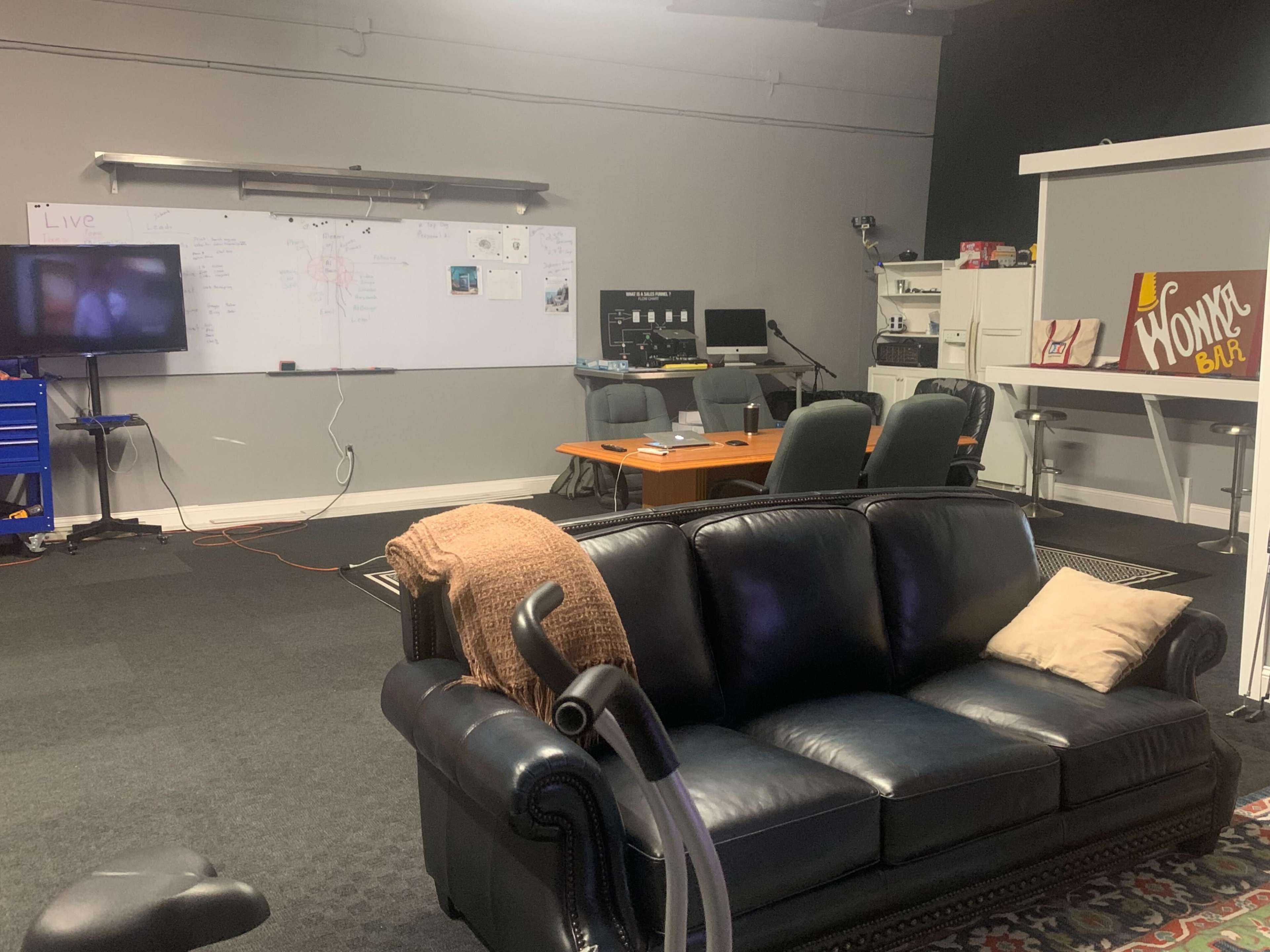 A modern office space with a black couch, a whiteboard filled with notes, and several workstations arranged around a central table.