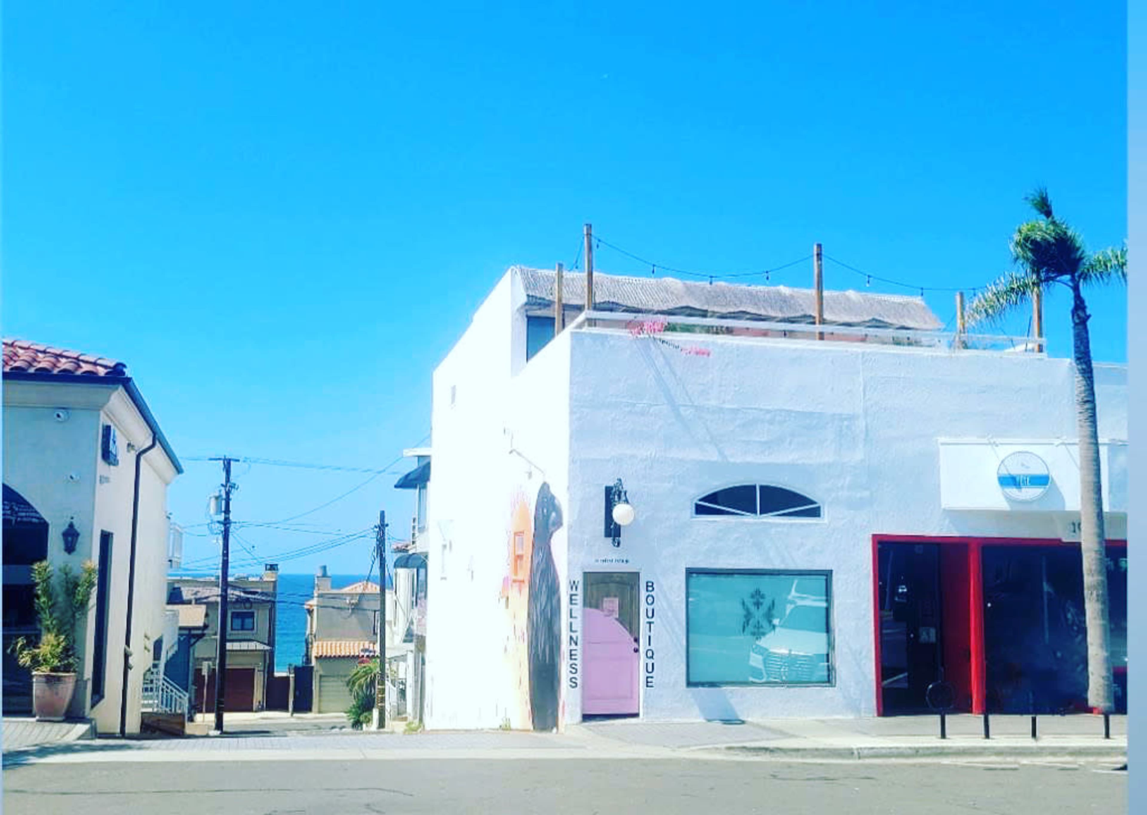 A colorful building in a sunny street, featuring a wellness boutique and a nearby palm tree.