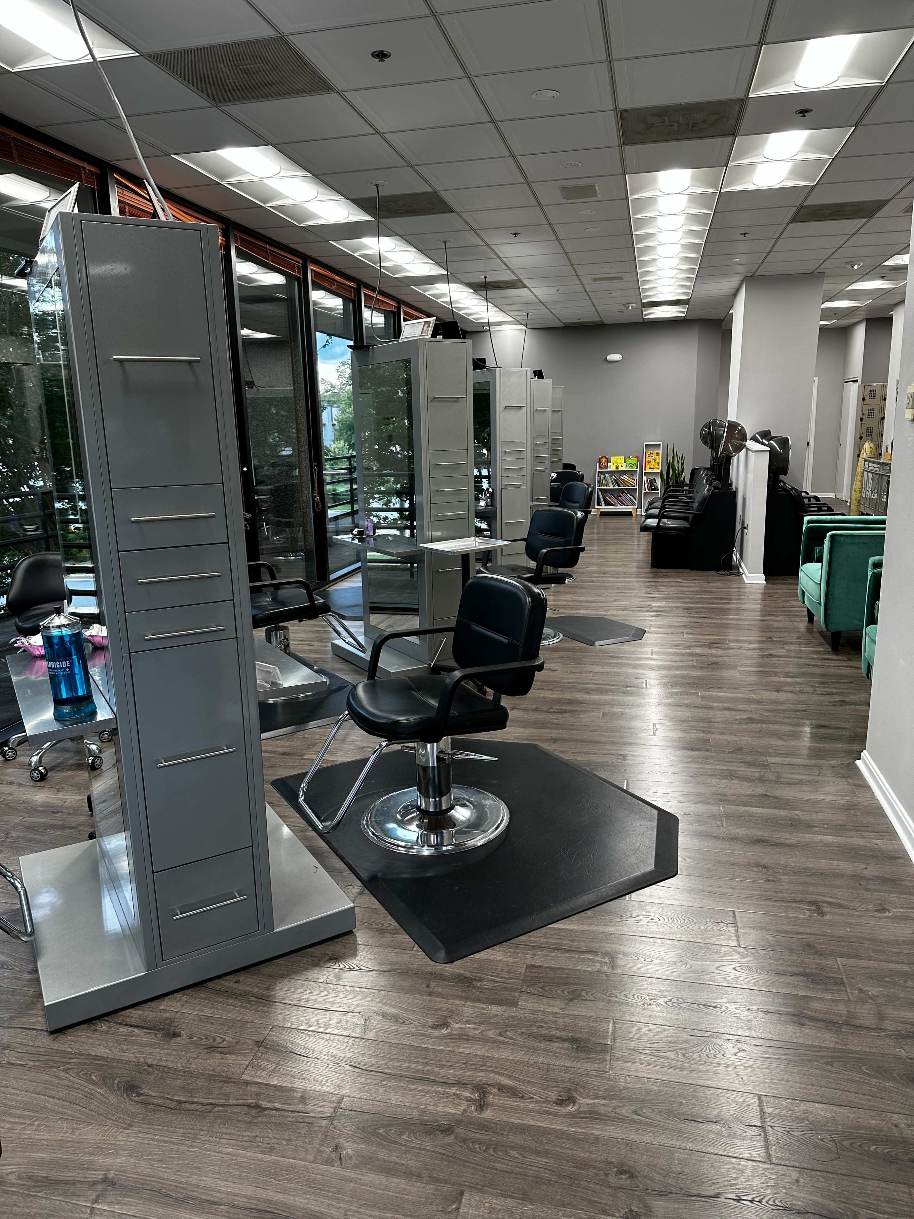 A hair salon interior with styling stations, black chairs, and a wooden floor.