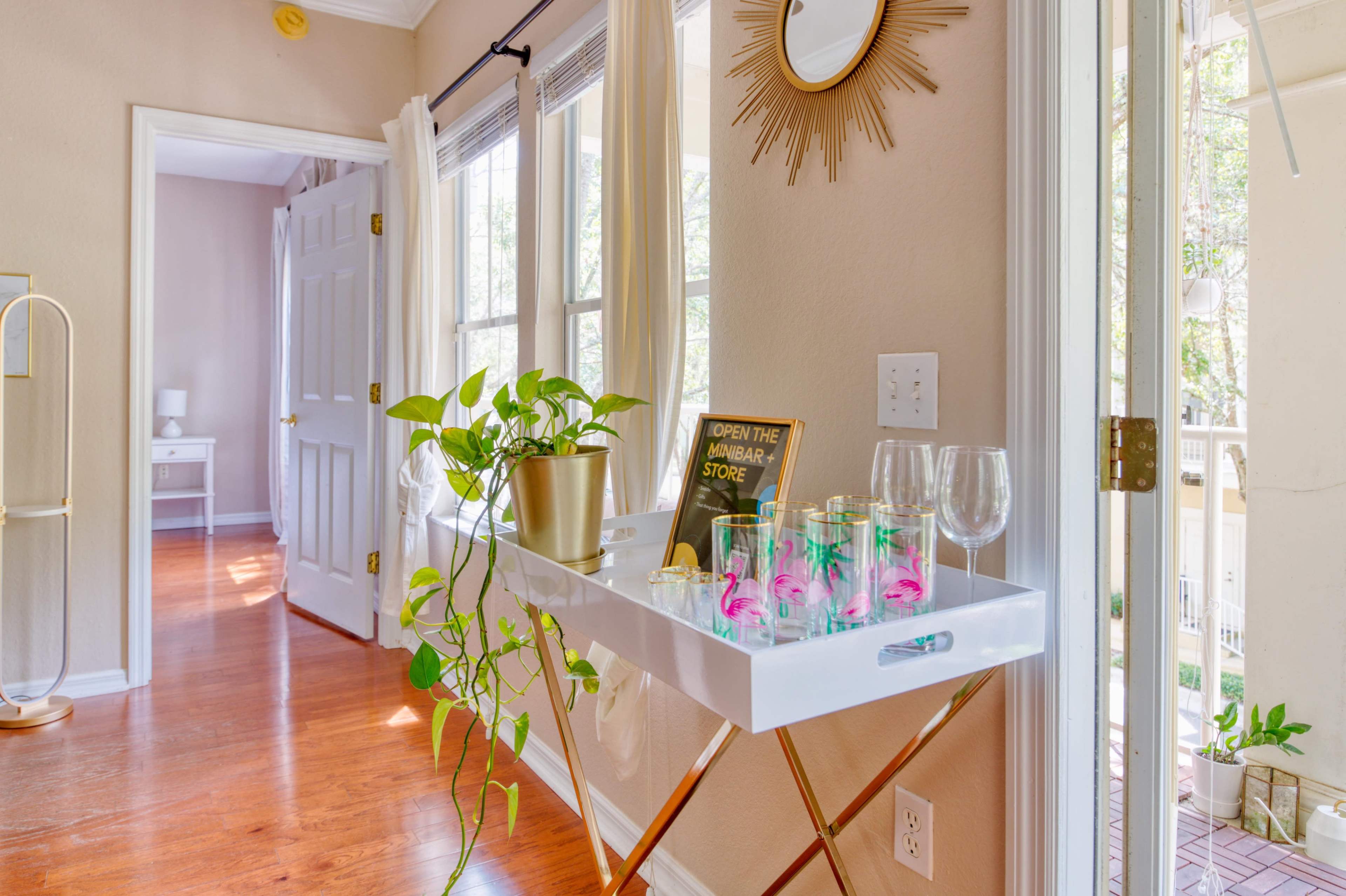 A white serving tray with glasses and a plant sits next to an open door, leading to a bright hallway with wooden flooring and a mirror on the wall.