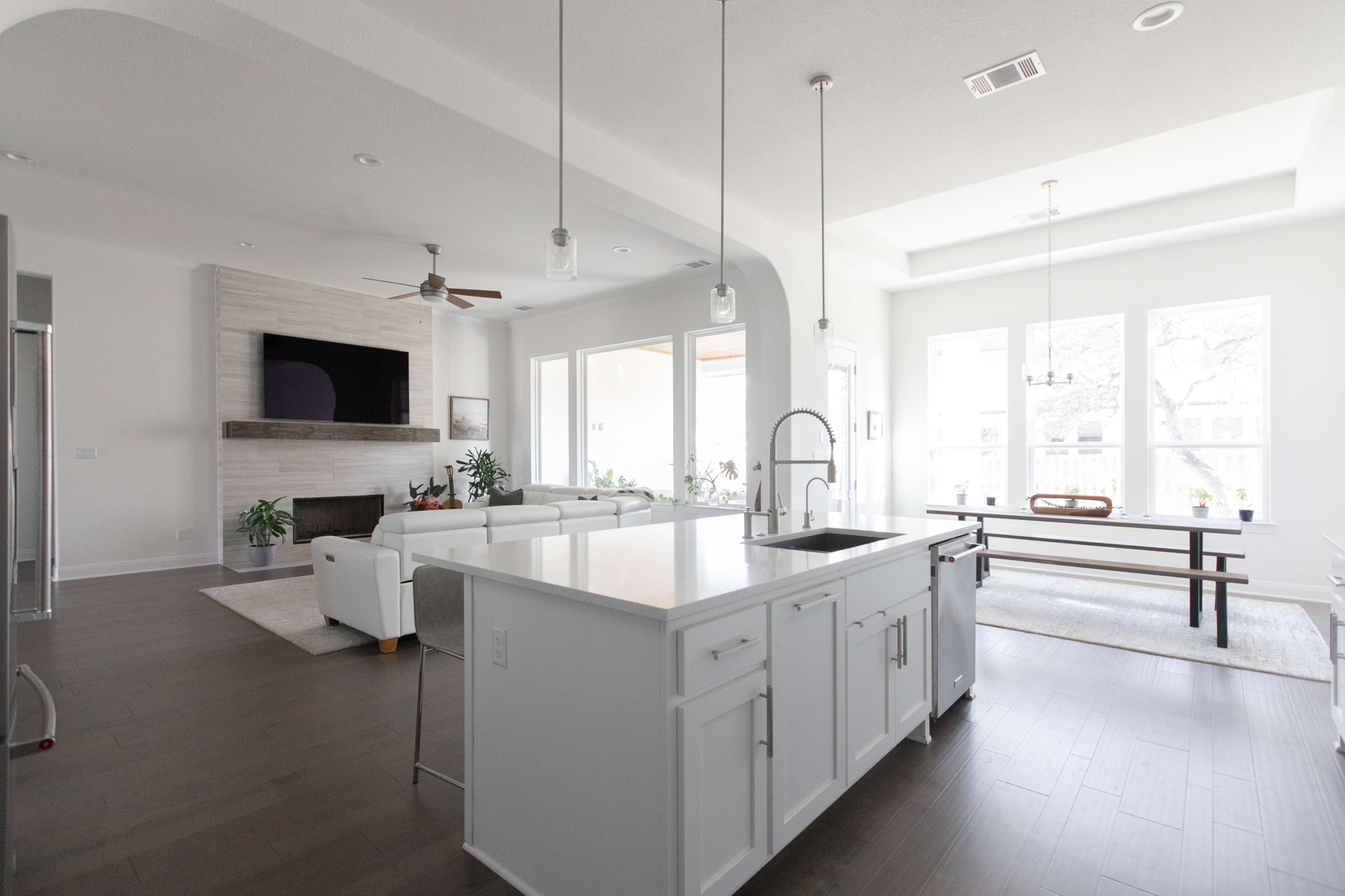 A modern open-concept living space featuring a kitchen with a central island, a dining area with a long table, and a living area with a fireplace and large windows.